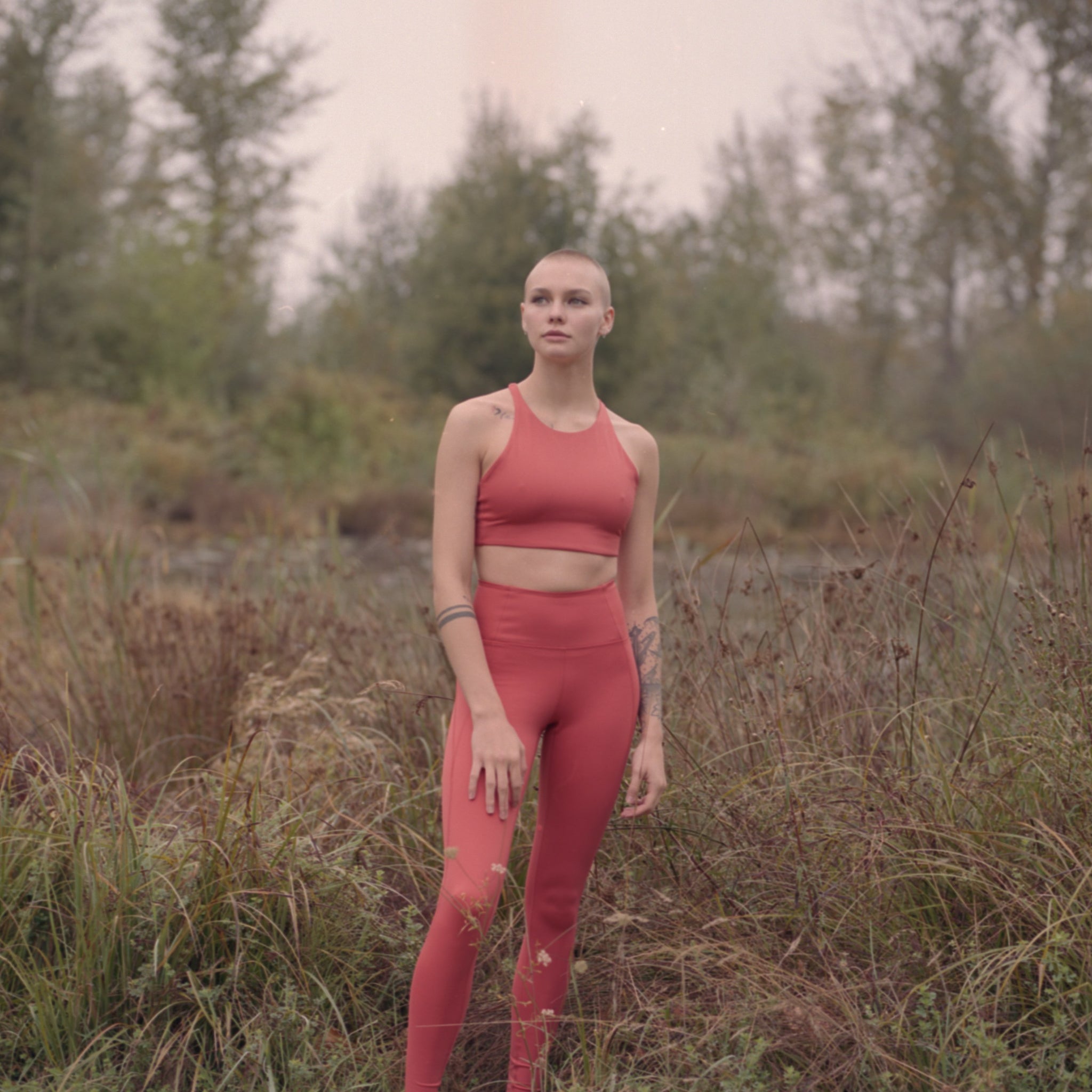 Eine Person in roter Sportkleidung steht auf einer Wiese in einem bewaldeten Gebiet.