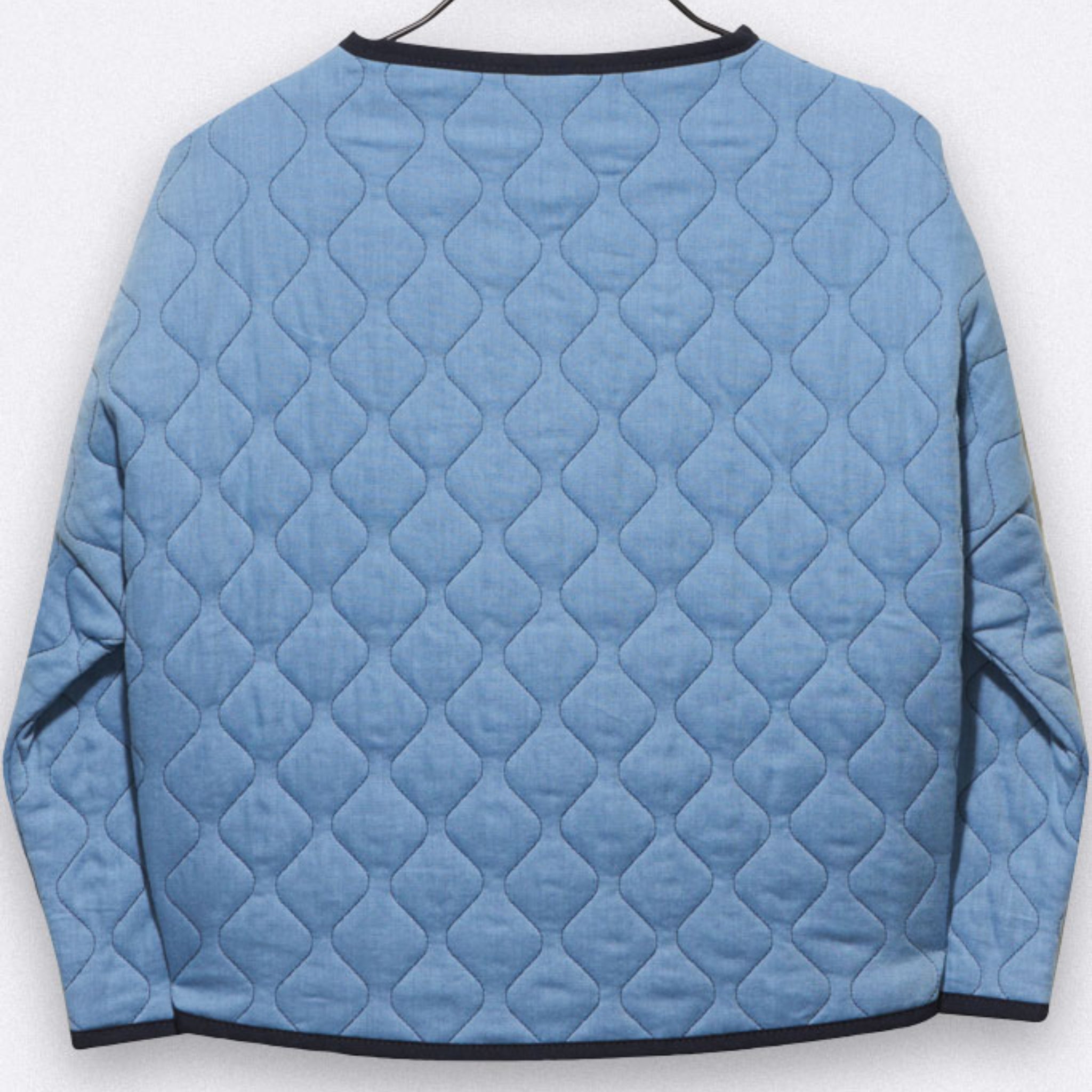 Eine hellblaue, gesteppte, langärmelige Jacke ist auf einem Bügel ausgestellt. Die Jacke weist ein rautenförmiges Steppmuster auf und hat dunkle Besätze am Hals, an den Manschetten und am Saum. Die Abbildung zeigt die Rückenansicht.