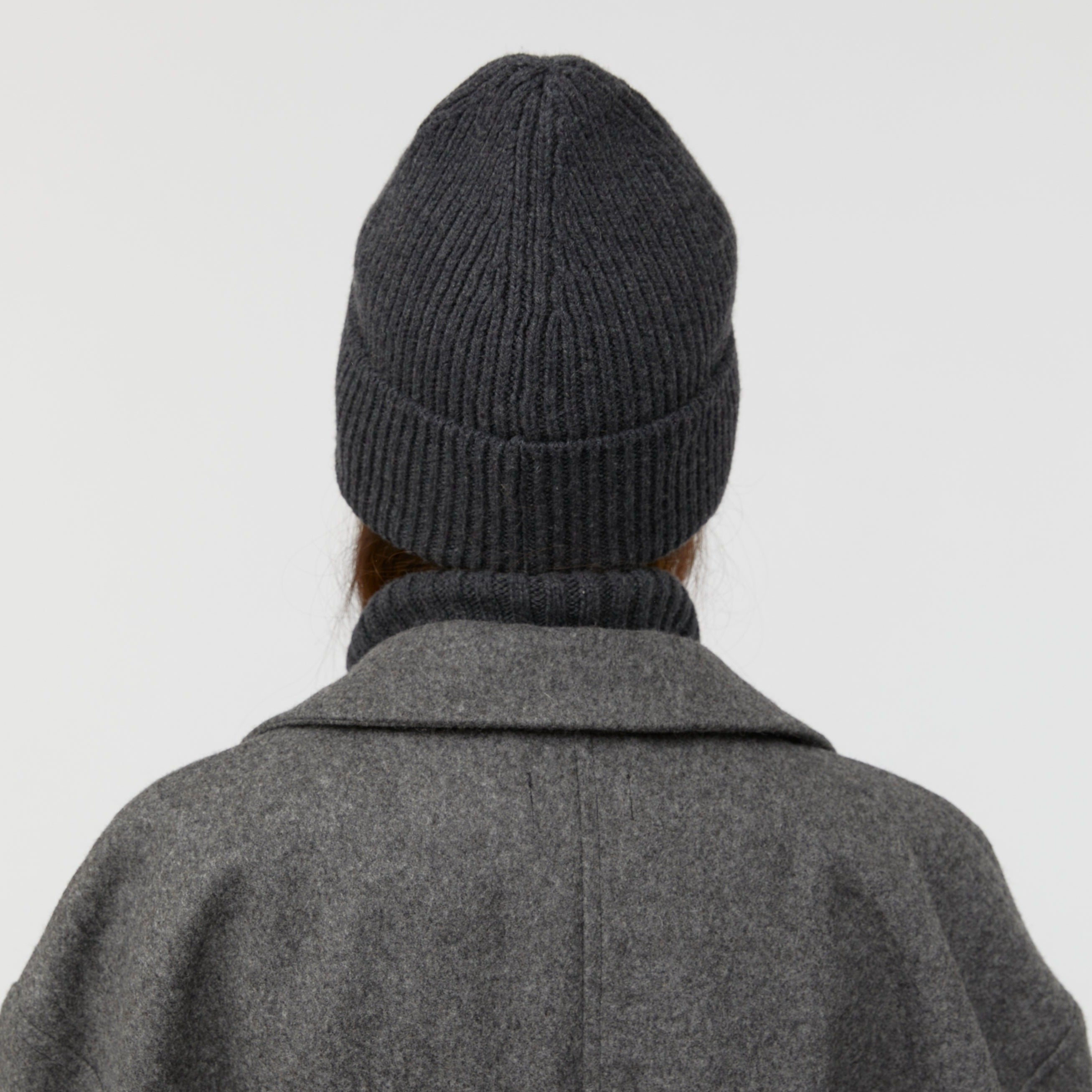 Person mit grauem Mantel und dunkelgrauer Strickmütze von hinten.
