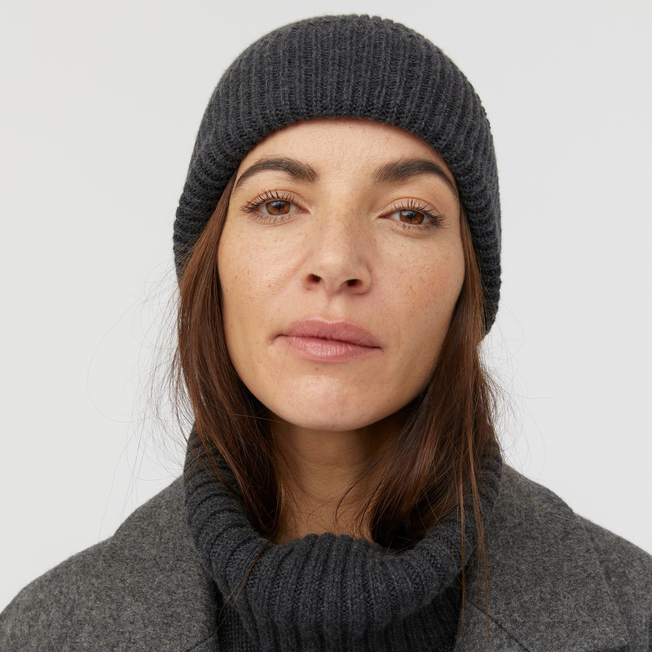 Frau mit grauem Strickmütze und grauem Rollkragenpullover blickt ernst in die Kamera.