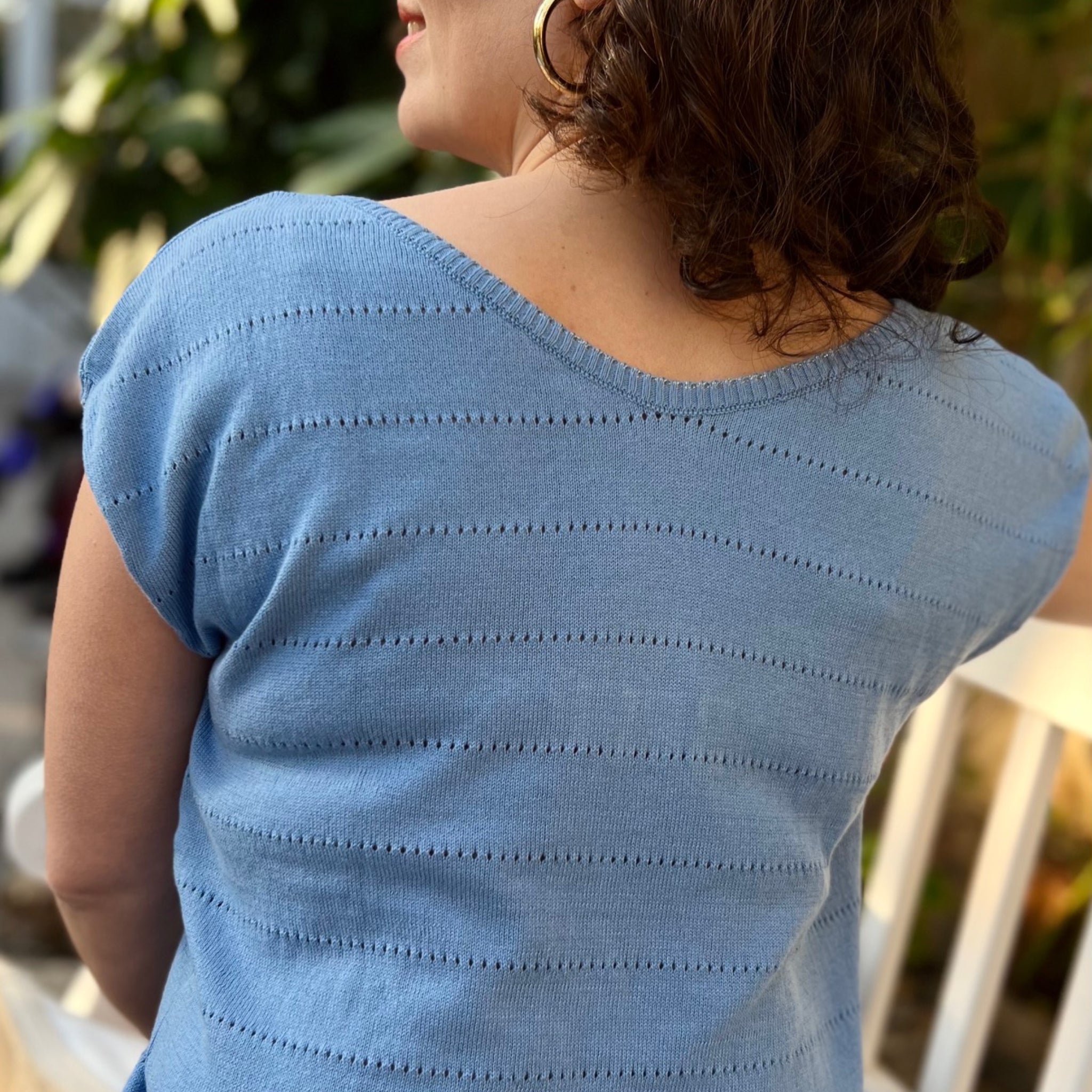 Eine Person mit lockigem Haar trägt ein blaues, gestreiftes Oberteil, von hinten fotografiert.