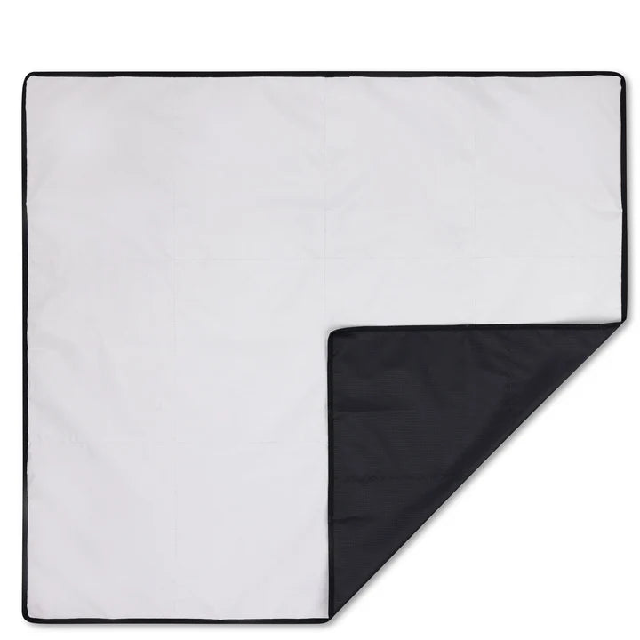 Eine quadratische Decke mit einer weißen Oberseite und einer schwarzen Unterseite. Eine Ecke ist umgeschlagen, damit die schwarze Unterseite sichtbar wird, und die Decke hat einen schwarzen Rand.