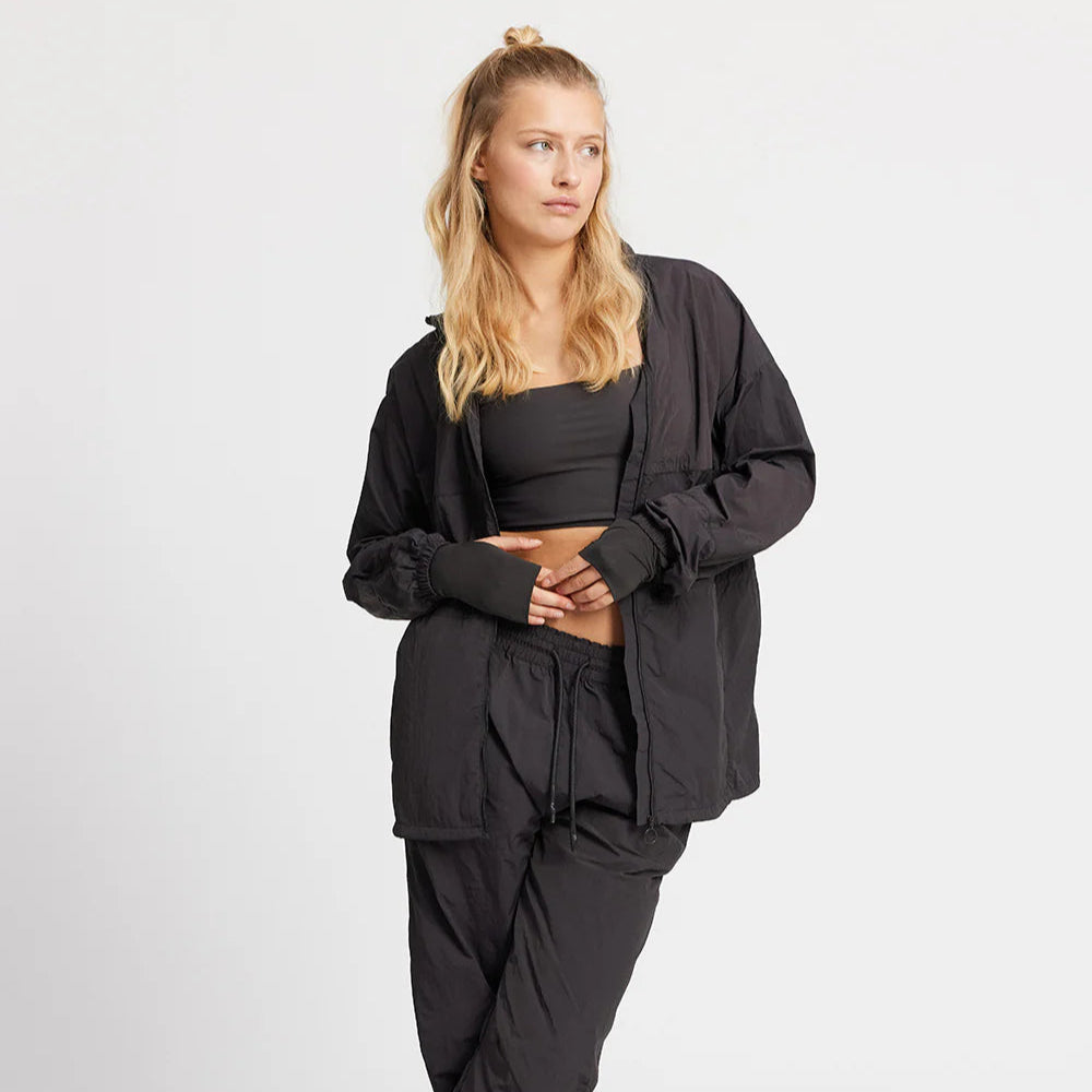 Frau mit langen blonden Haaren trägt ein schwarzes Sportoutfit und blickt zur Seite.