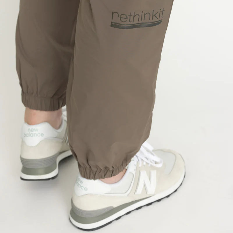 Nahaufnahme einer Person, die eine taupefarbene Jogginghose mit dem Aufdruck "rethinkit" am Bein trägt, gepaart mit weißen und grauen New Balance Turnschuhen.