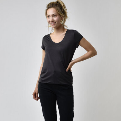 Frau in schwarzem T-Shirt und Hose, lächelnd und seitlich stehend vor neutralem Hintergrund.