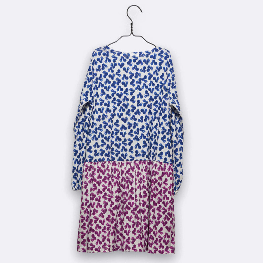 Ein langärmeliges Kleid hängt auf einem Kleiderbügel. Die obere Hälfte ist mit einem blau-weißen Blumenmuster versehen, während die untere Hälfte in ein lila-weißes Blumenmuster übergeht. Der Hintergrund ist einfarbig und hell.