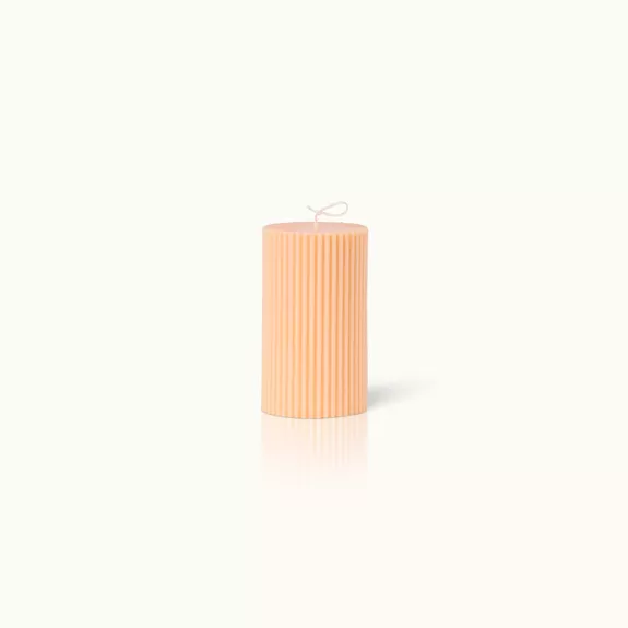 Gerippte, orangefarbene Stumpenkerze auf hellem Hintergrund.