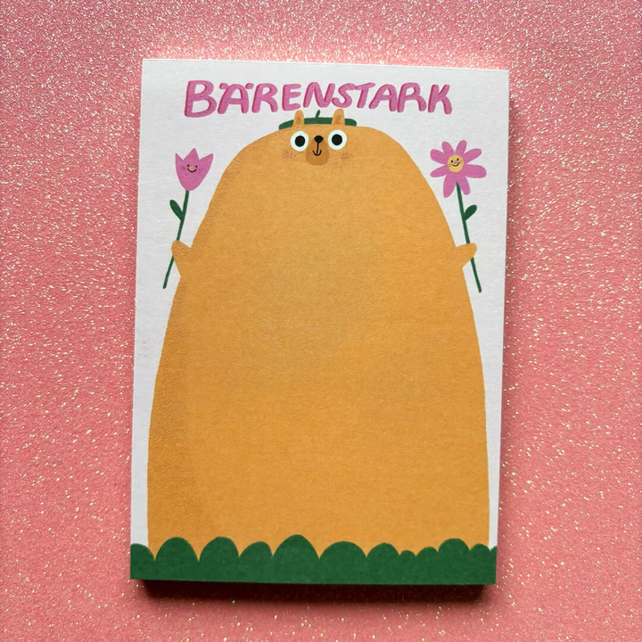 Eine niedliche Illustration eines großen, gelben Bären, der rosa Blumen hält, mit dem Wort BÄRENSTARK darüber, vor einem rosa glitzernden Hintergrund.