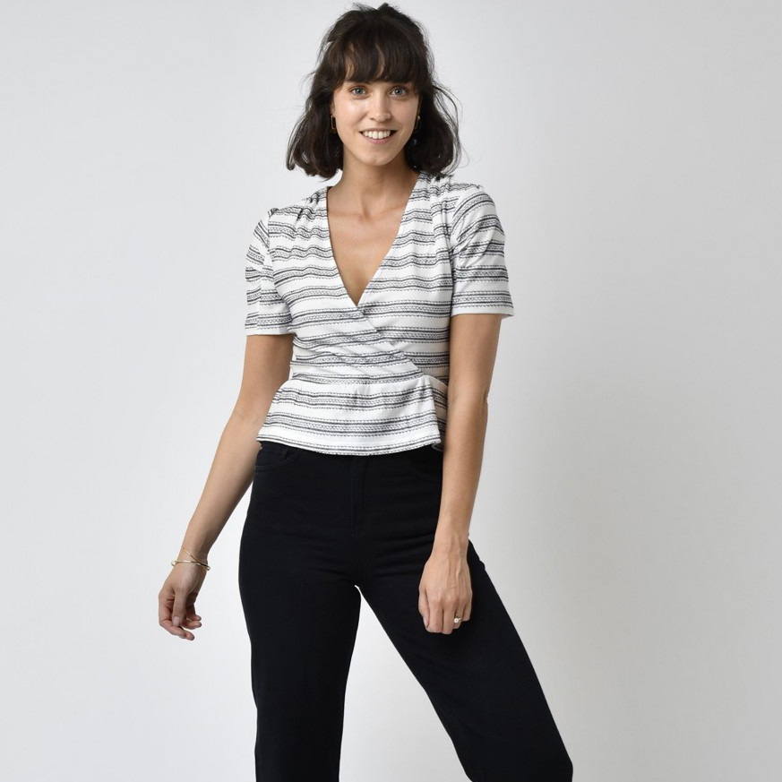 Frau in gestreiftem Oberteil und schwarzer Hose lächelt in die Kamera.