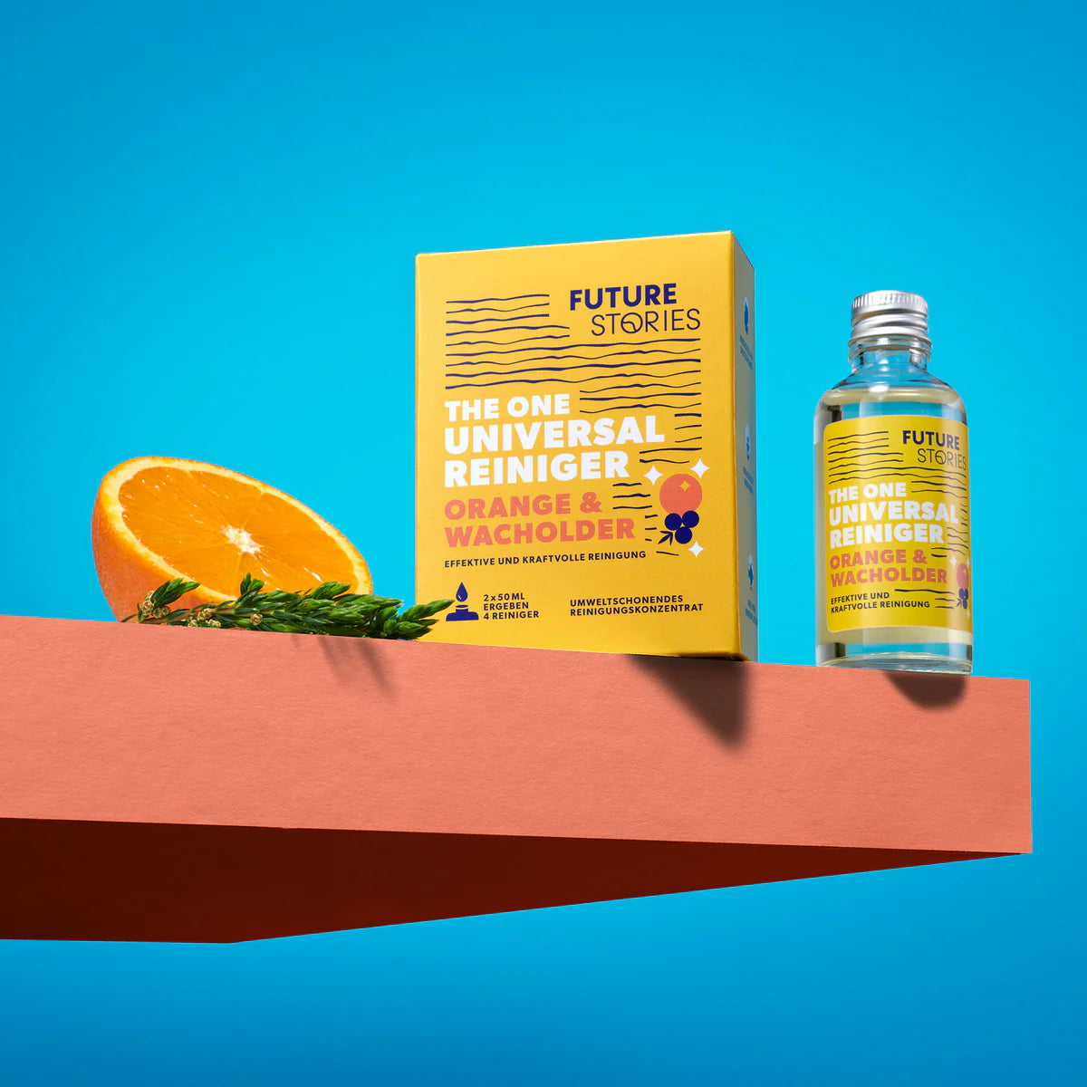 Eine Schachtel und eine Flasche Future Stories The One Universal Reiniger Orange & Wacholder werden auf einer rosa Fläche mit einer Orangenscheibe und Rosmarinzweigen vor einem leuchtend blauen Hintergrund präsentiert.