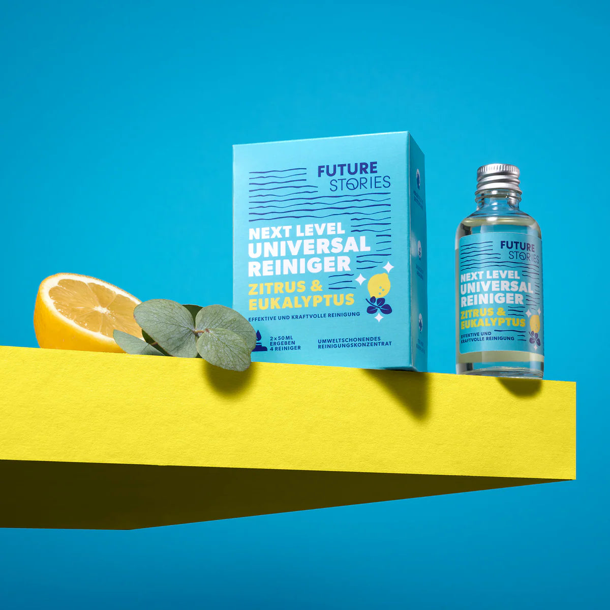Eine Flasche und eine Schachtel Future Stories Next Level Universal Reiniger Zitrus & Eukalyptus stehen auf einem gelben Regal mit einer Zitronenhälfte und Eukalyptusblättern vor einem hellblauen Hintergrund.