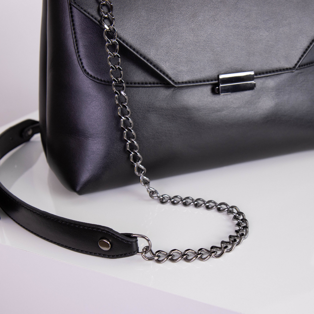 Schwarze Ledertasche mit silberner Gliederkette auf weißem Hintergrund.