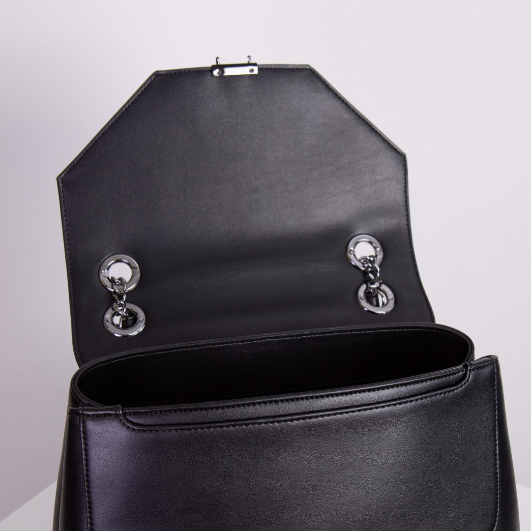 Geöffnete schwarze Ledertasche mit silbernen Kettendetails auf hellem Hintergrund.