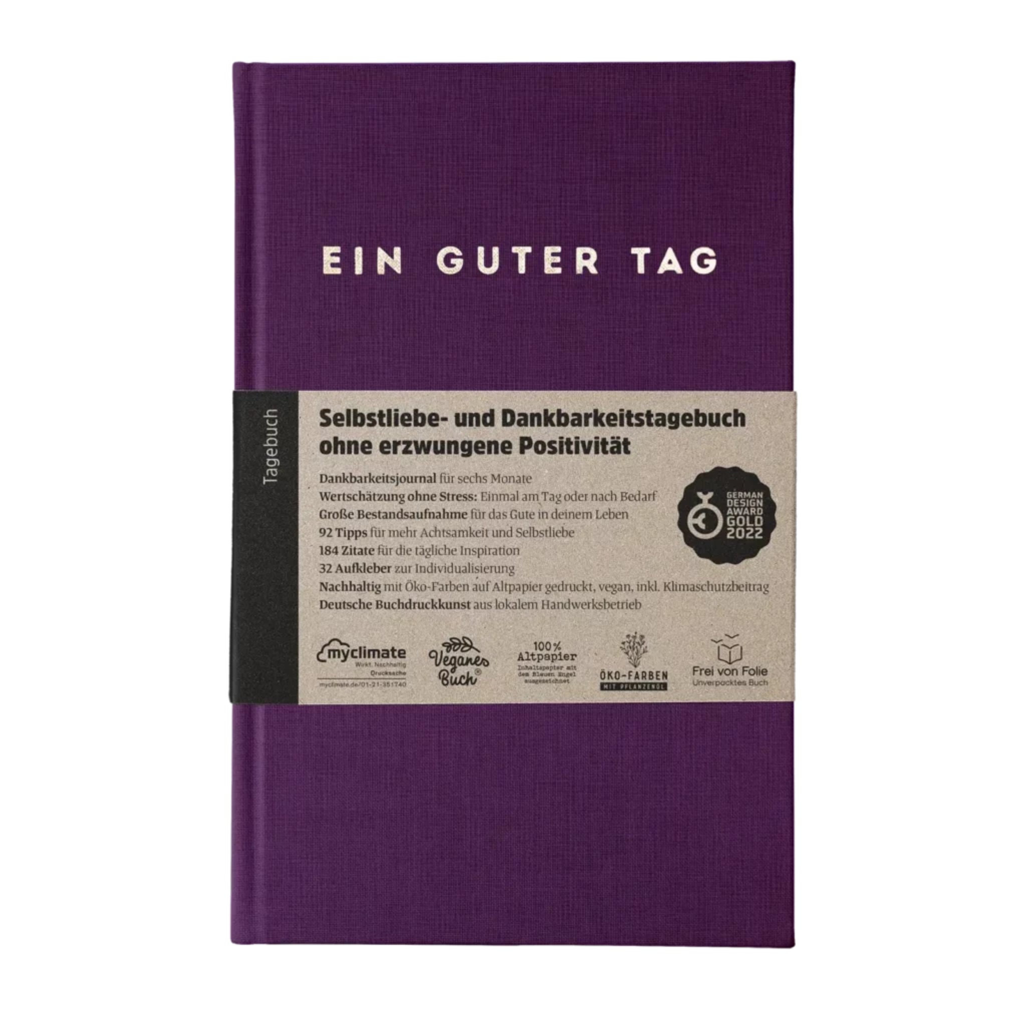Lila Tagebuch mit der Aufschrift „EIN GUTER TAG“ und Banderole mit Infos zu Selbstliebe, Dankbarkeit und Nachhaltigkeit.