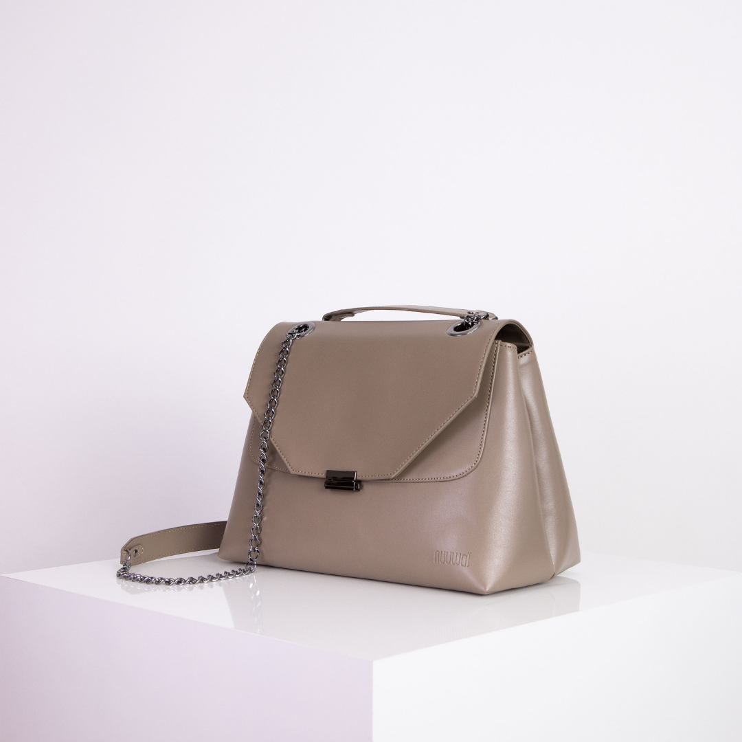 Graue Handtasche mit Kettengurt auf weißem Tisch vor weißem Hintergrund.