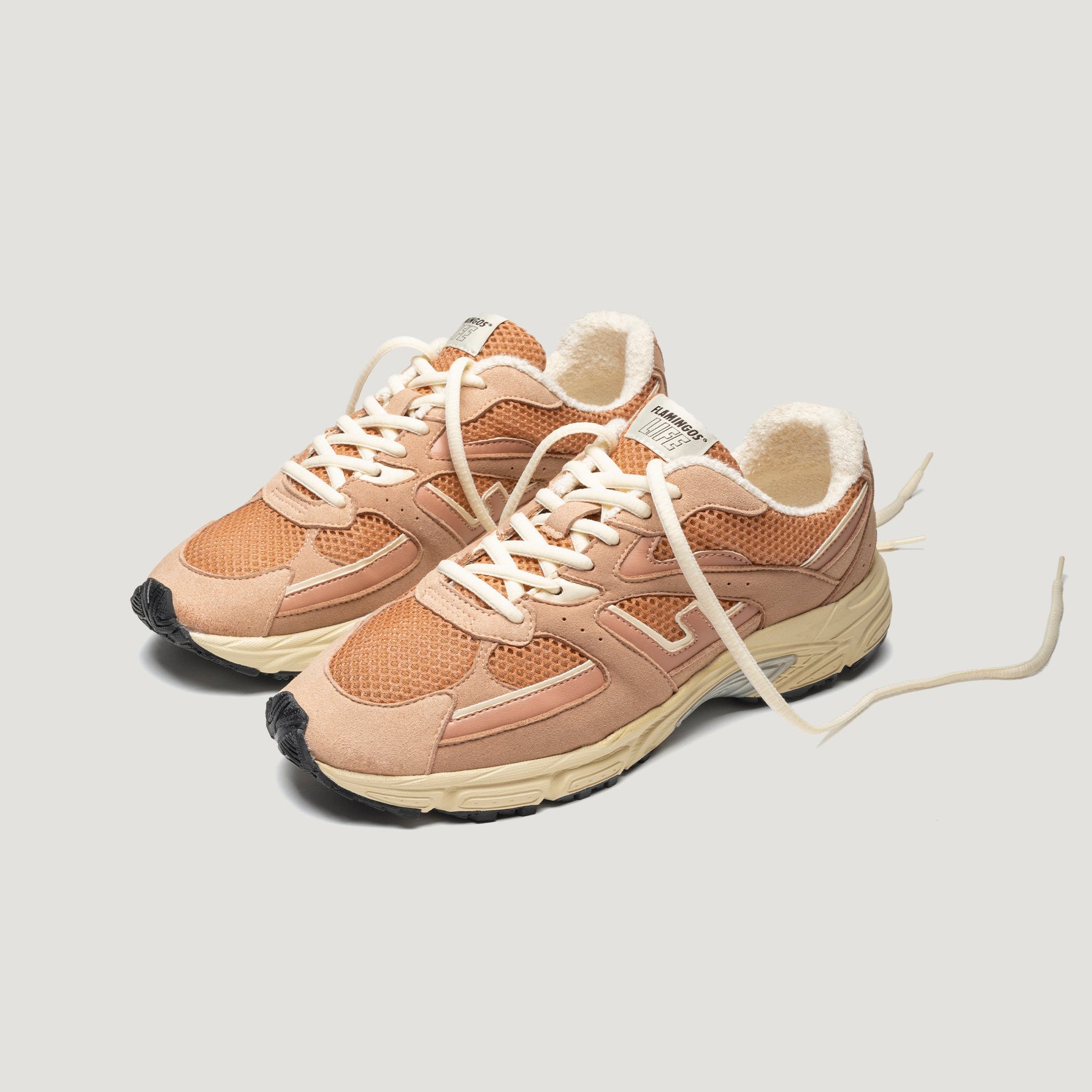 Ein Paar hellbraune und beigefarbene Turnschuhe mit weißen Schnürsenkeln, Obermaterial aus Mesh und klobigen cremefarbenen Sohlen auf einem hellgrauen Hintergrund.