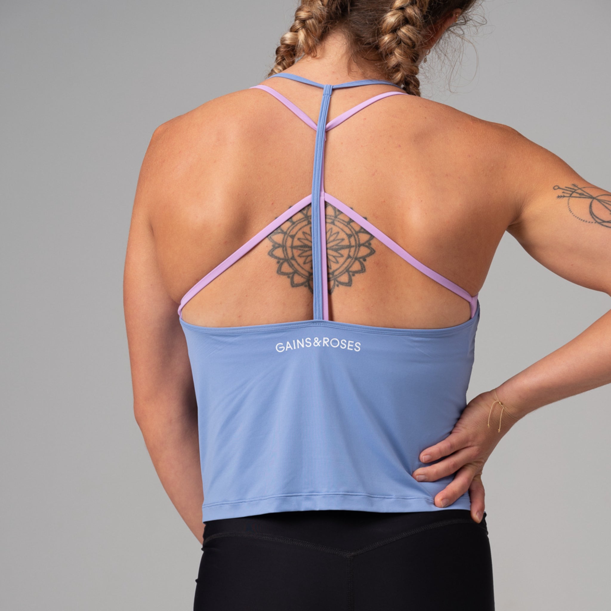 Frau von hinten in blauem Top mit lila Trägern und Mandala-Tattoo auf dem Rücken.