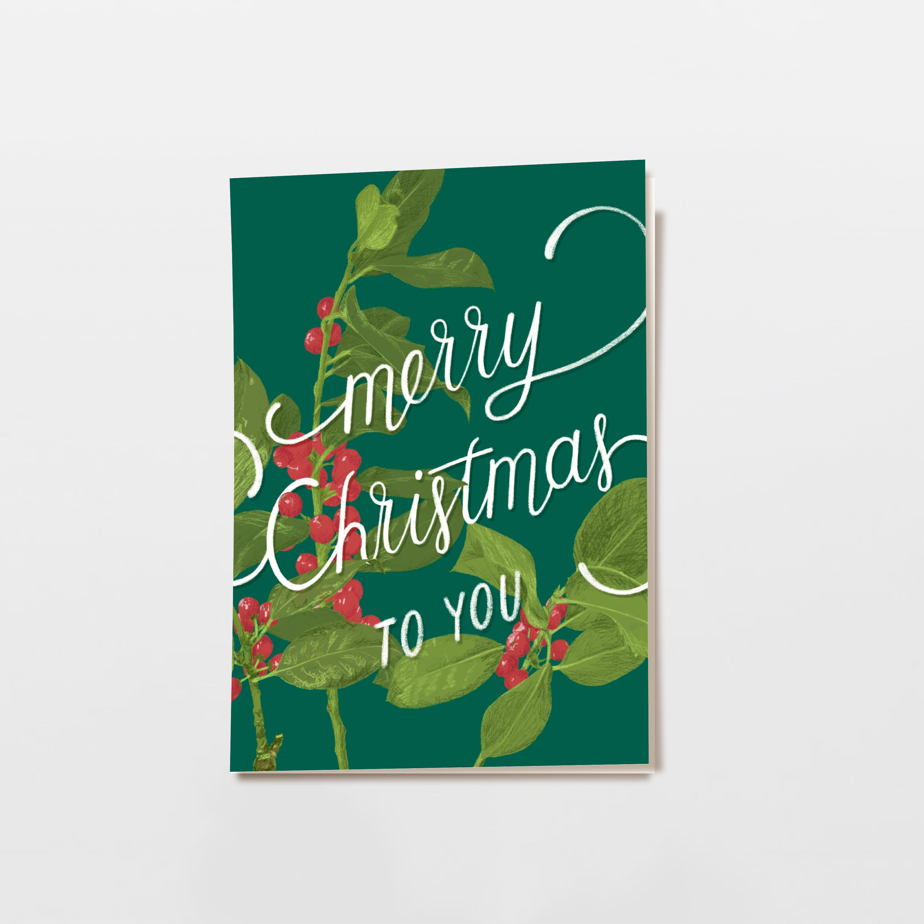 Eine grüne Grußkarte mit Stechpalmenblättern und roten Beeren, mit dem weißen handgeschriebenen Text Merry Christmas to you.