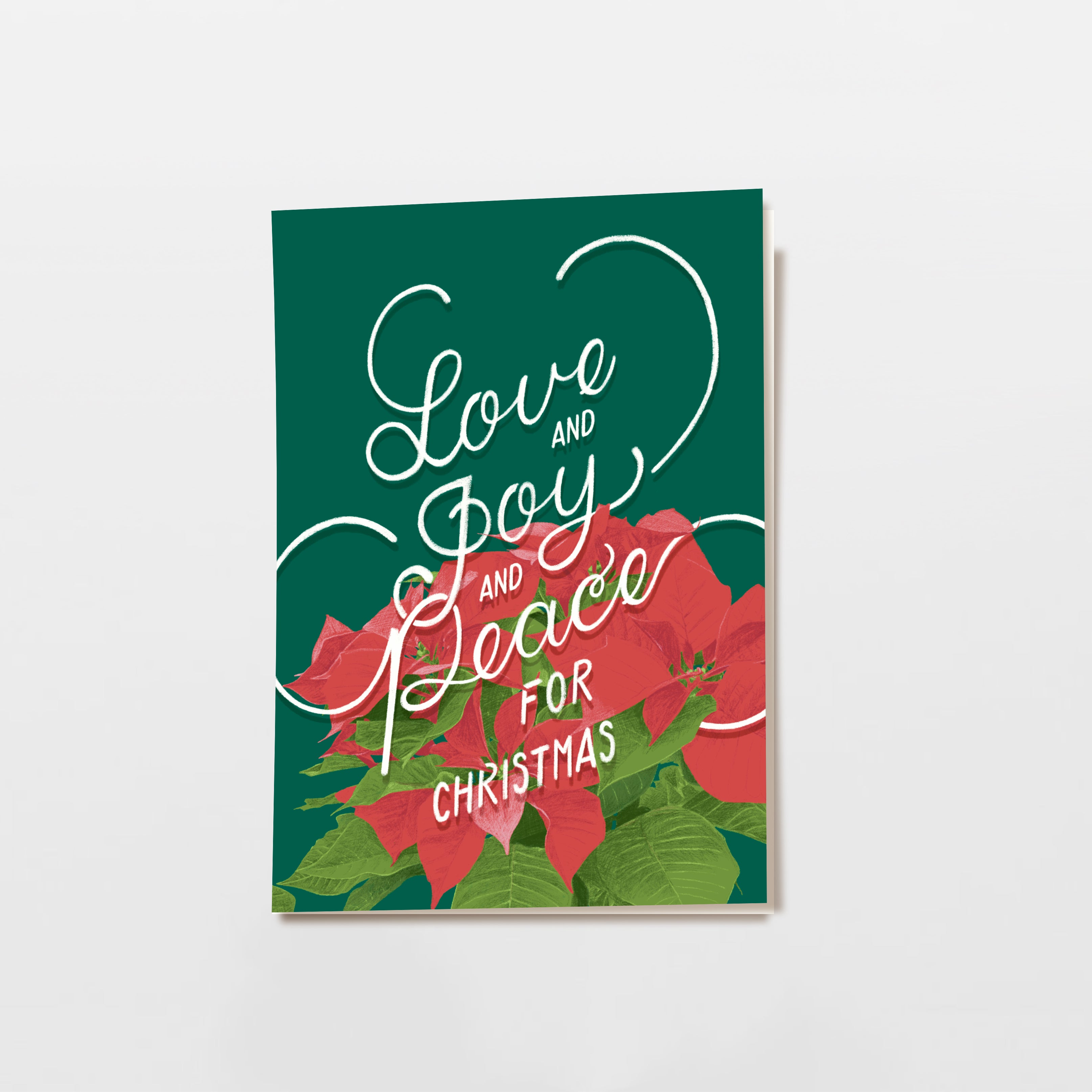 Eine Weihnachtskarte mit roten Weihnachtssternblüten und der handgeschriebenen Botschaft Love and Joy and Peace for Christmas auf dunkelgrünem Hintergrund.