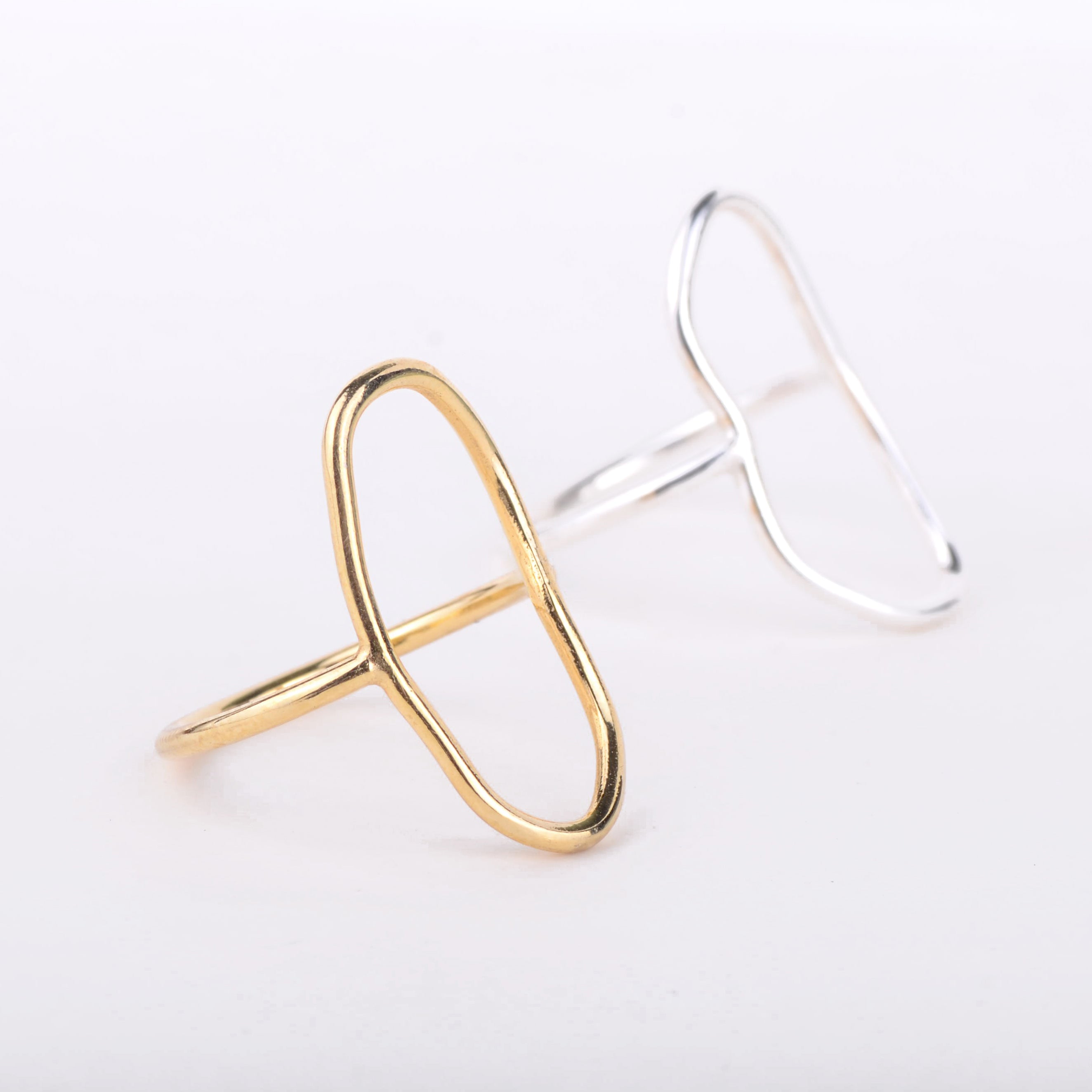 Zwei minimalistische Ringe, ein goldener und ein silberner, jeder mit einer abstrakten, offenen ovalen Form, sind auf einem weißen Hintergrund dargestellt. Der goldene Ring befindet sich im Vordergrund und der silberne Ring etwas dahinter.