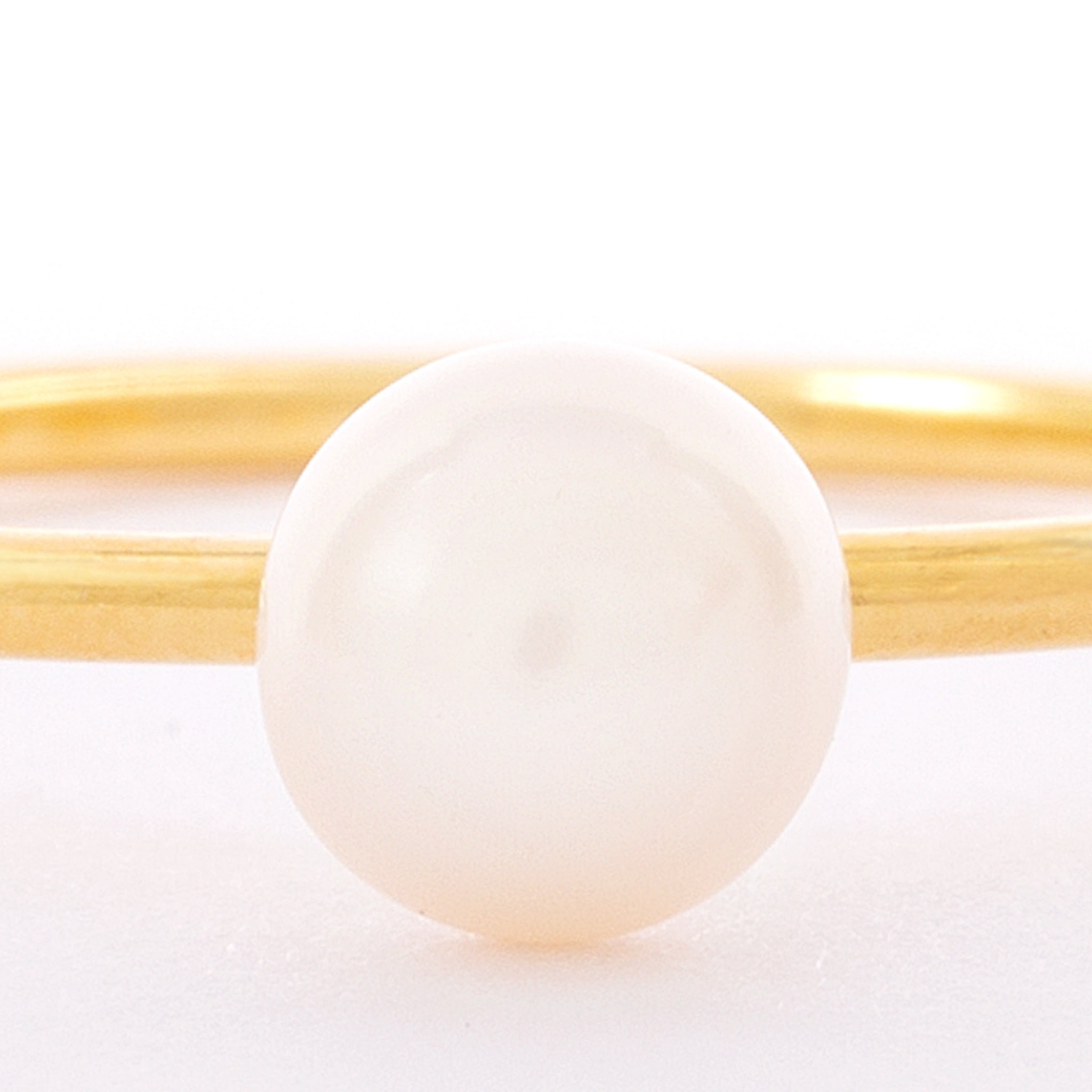 Nahaufnahme eines Goldrings mit einer einzelnen, runden weißen Perle in der Mitte vor weißem Hintergrund.