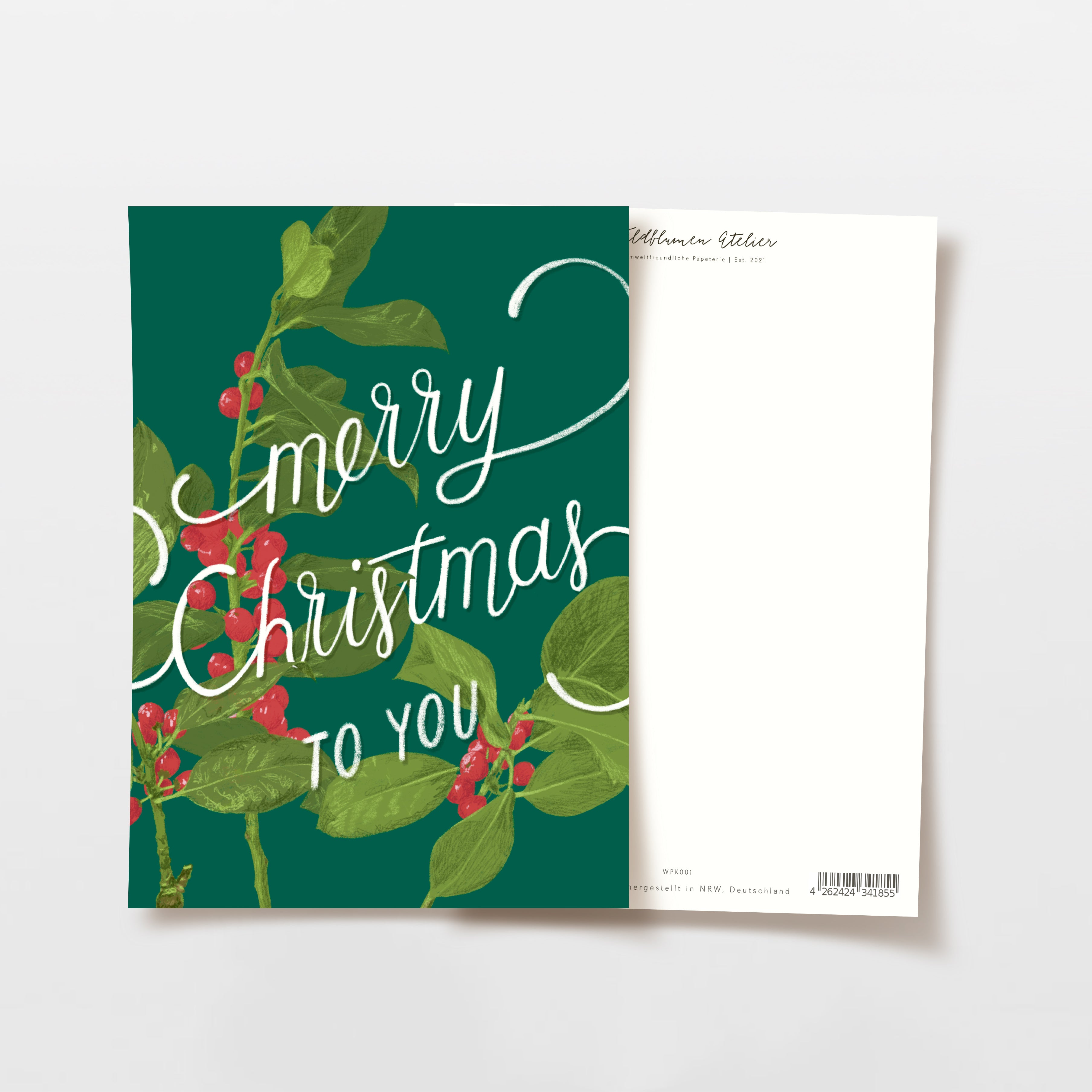 Eine Weihnachtskarte mit der Aufschrift "Merry Christmas to You" in weißer Schrift auf grünem Grund mit Stechpalmenblättern und roten Beeren, daneben eine leere weiße Rückseite mit einem Strichcode und einem kleinen gedruckten Text.