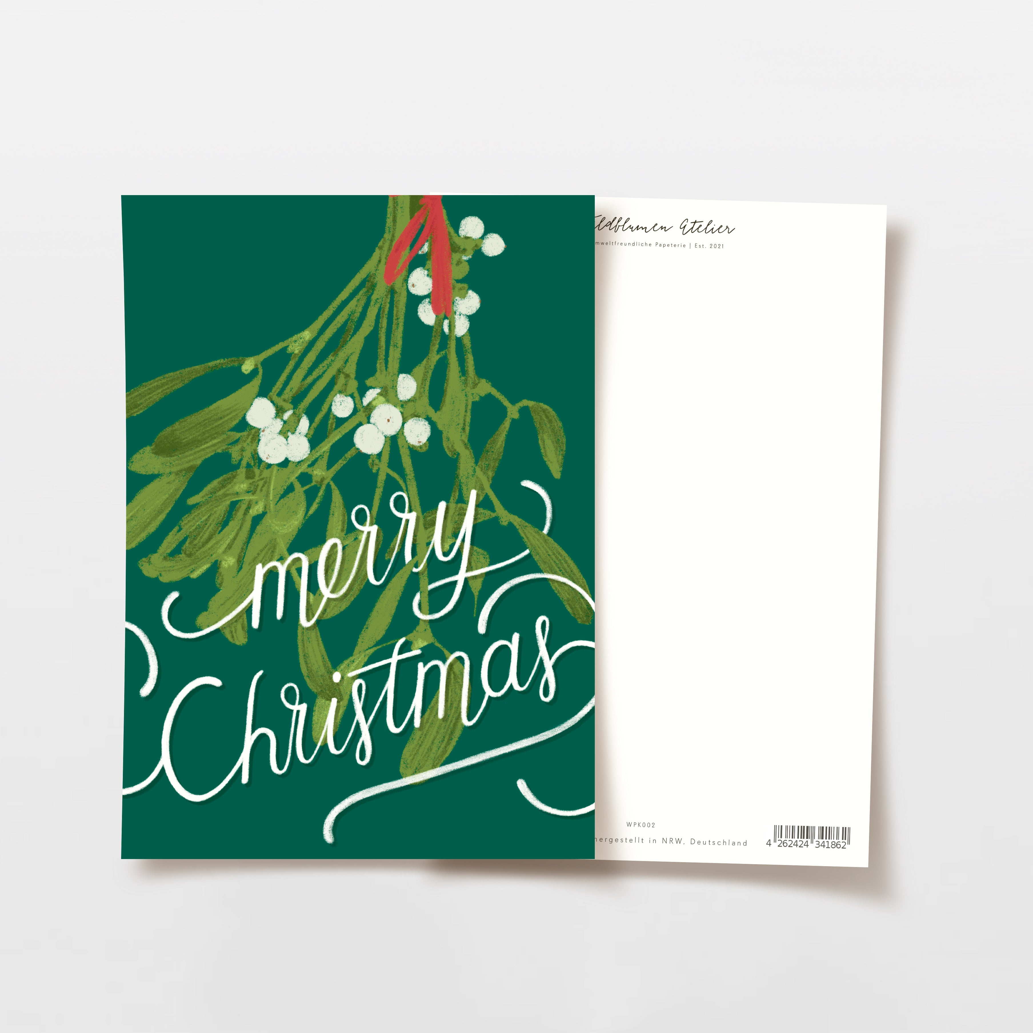 Eine Grußkarte mit einem illustrierten Mistelzweig und den Worten Frohe Weihnachten in weißer Schrift auf grünem Hintergrund. Die Rückseite der Karte ist größtenteils weiß mit Text am oberen Rand.