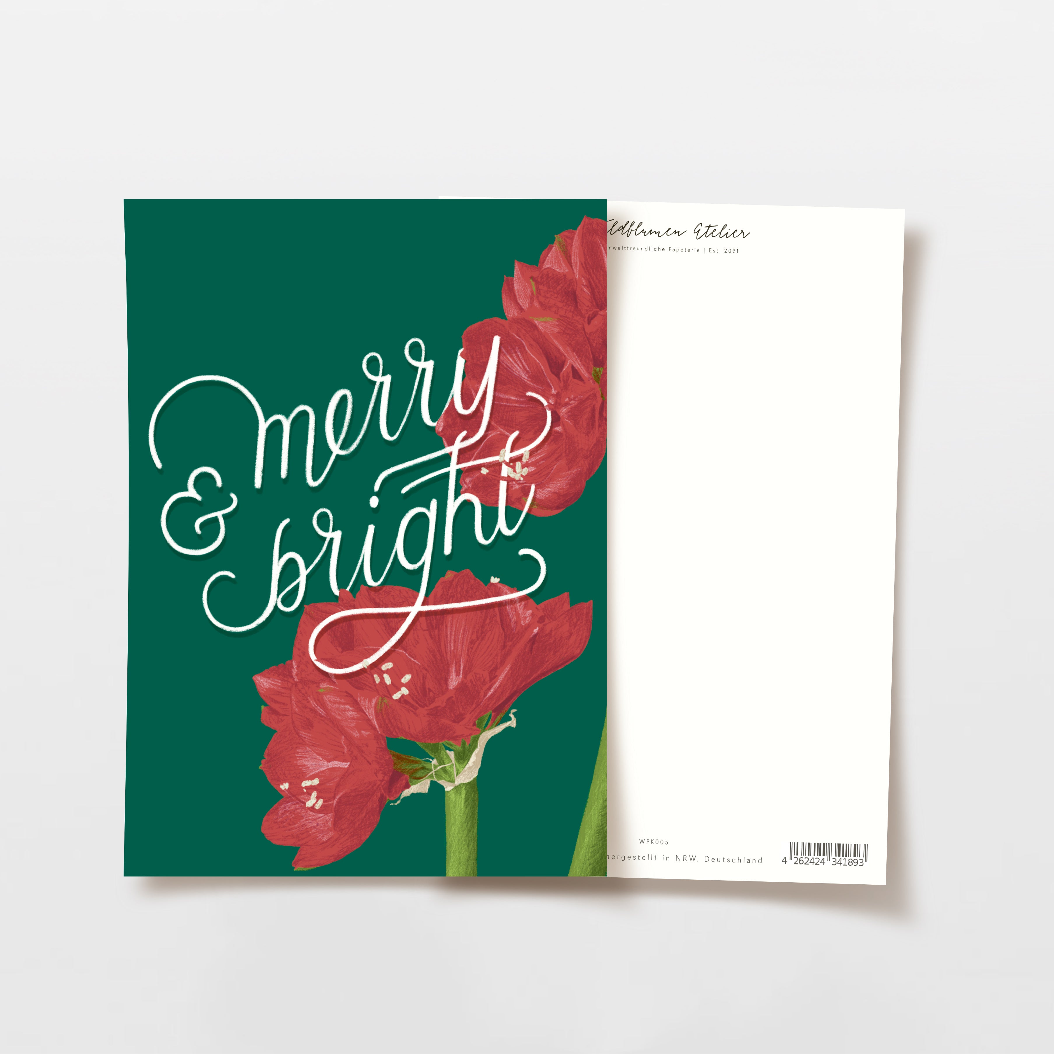Teilweise geöffnete Grußkarte mit der Aufschrift "merry & bright" in weißer Schrift auf dunkelgrünem Hintergrund mit roten Amaryllisblüten. Die Rückseite der Karte ist weiß mit kleinem Text am oberen Rand.