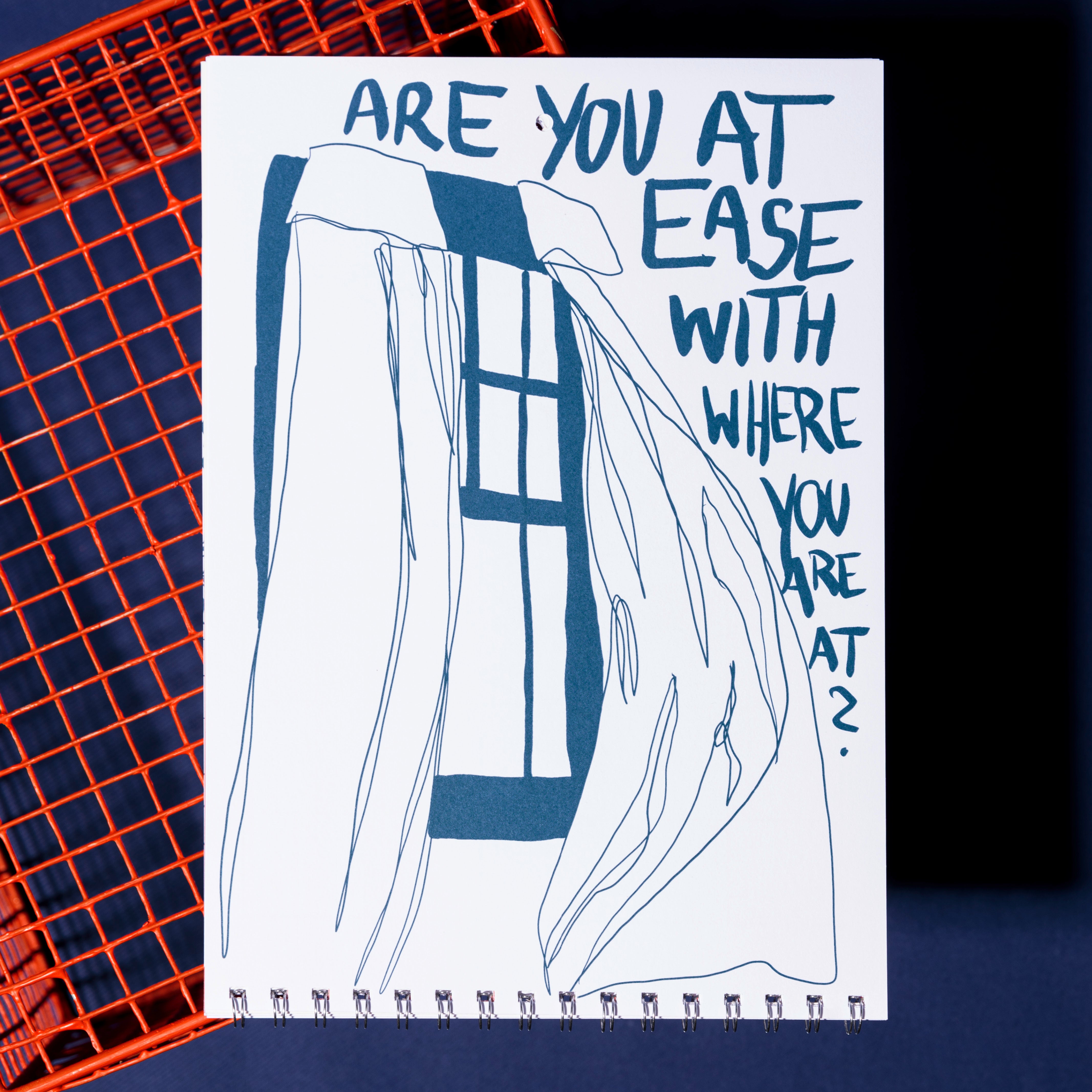 Eine Skizzenbuchseite mit einer blauen Strichzeichnung eines offenen Fensters und wehenden Vorhängen. Der Text lautet: Fühlst du dich wohl, wo du bist? Das Skizzenbuch ruht auf einem orangefarbenen Metallgitter vor einem dunkelblauen Hintergrund.