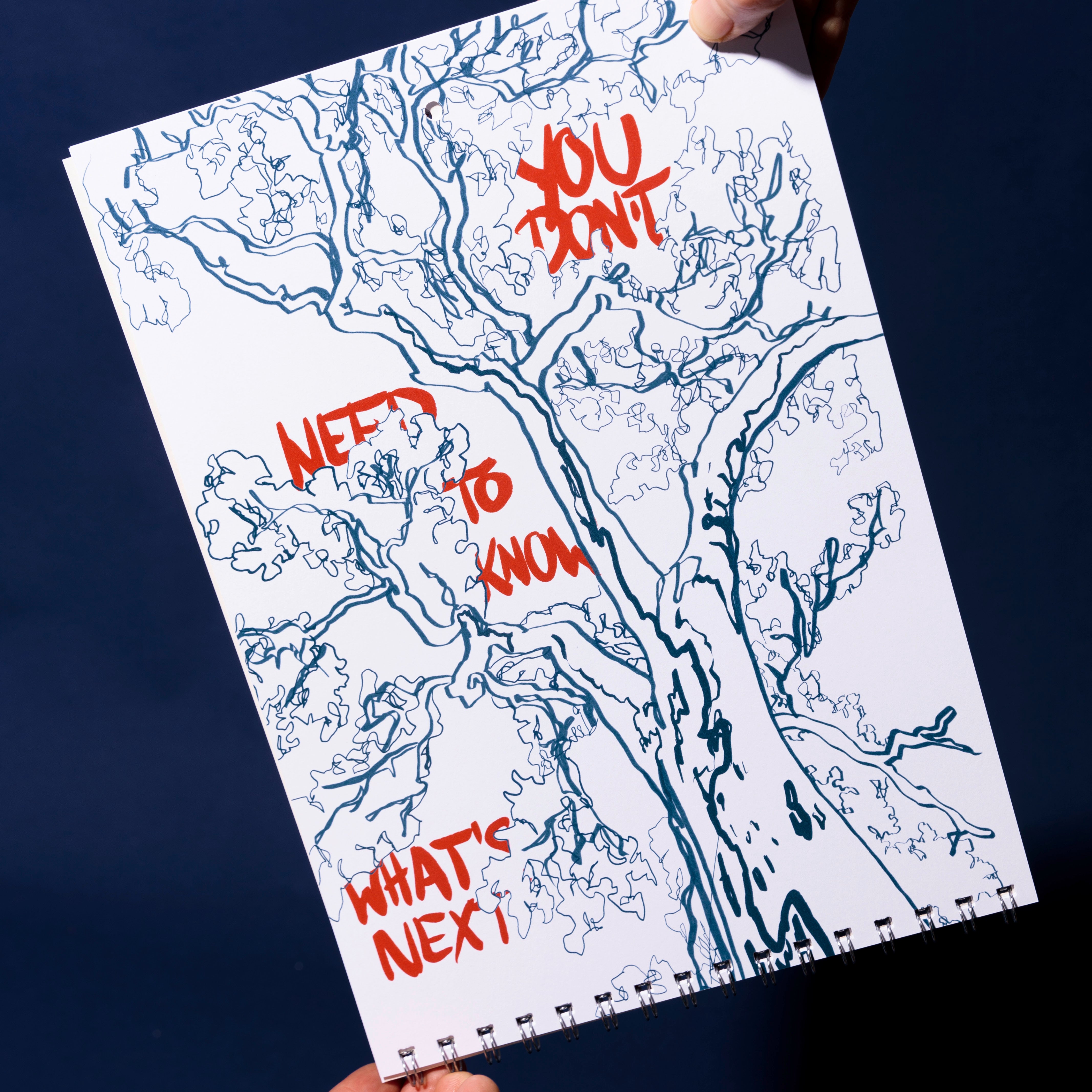 Eine Person hält ein Skizzenbuch mit einer detaillierten blauen Strichzeichnung eines Baumes. Über der Zeichnung steht in fetter roter Schrift: DU BRAUCHST NICHT ZU WISSEN, WAS ALS NÄCHSTES KOMMT. Der Hintergrund ist dunkelblau.