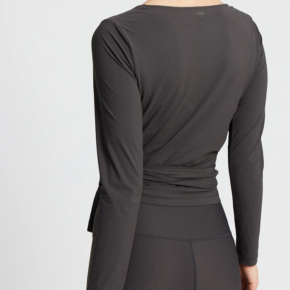Person in einem langärmeligen, dunkelgrauen Sporttop und Leggings von hinten zu sehen.