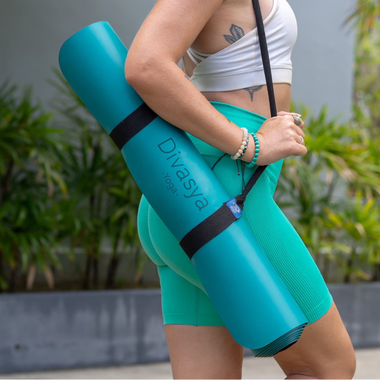 Frau trägt eine zusammengerollte türkisfarbene Yogamatte auf der Schulter und trägt passende Sportbekleidung.