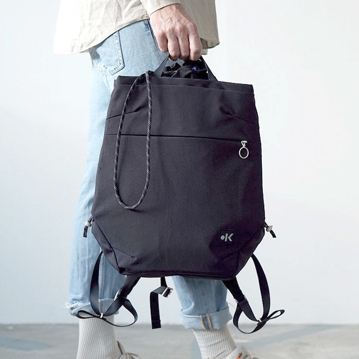 Person trägt einen schwarzen Rucksack, trägt hellblaue Jeans und cremefarbene Schuhe.