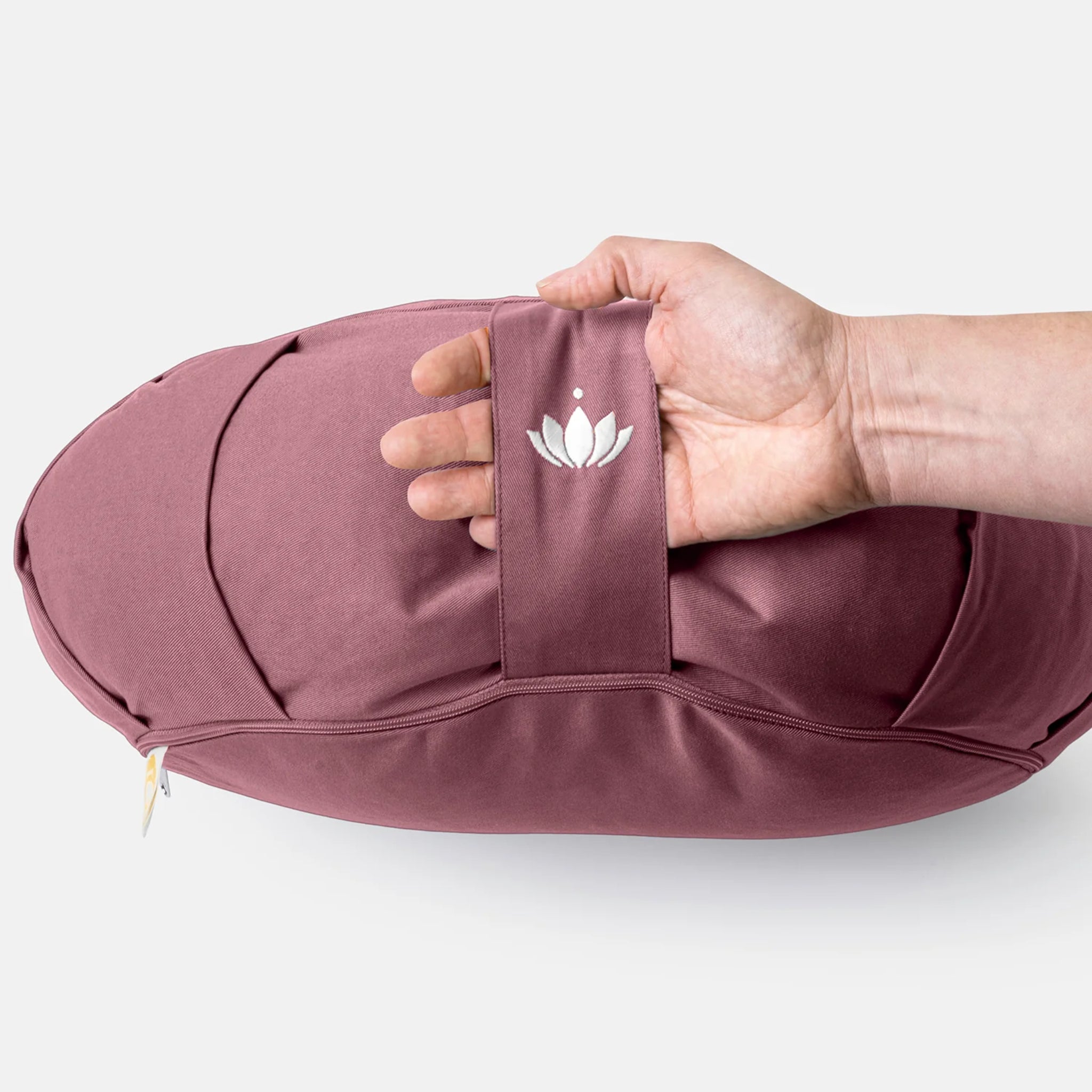 Eine Hand hält ein rosafarbenes Kissen mit einem Tragegriff, der mit einem Lotus-Symbol bestickt ist.