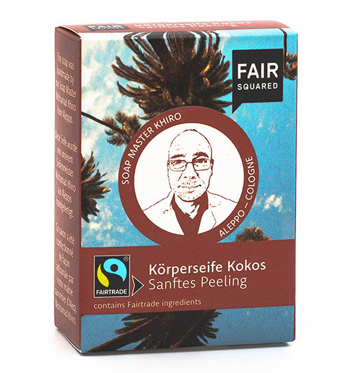 Eine Schachtel Fair Squared Körperseife Kokos mit dem gezeichneten Porträt einer Person, einem Palmenmotiv und dem Fairtrade-Logo sowie einem Text in Deutsch und Englisch über Kokosnuss-Körperseife und sanftes Peeling.