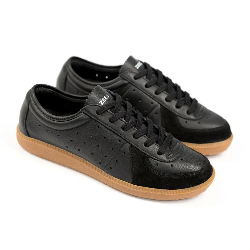 Ein Paar schwarzer Ledersneakers mit perforierten Seiten, schwarzen Schnürsenkeln, Wildlederdetails und hellbraunen Gummisohlen, schräg betrachtet auf weißem Hintergrund.