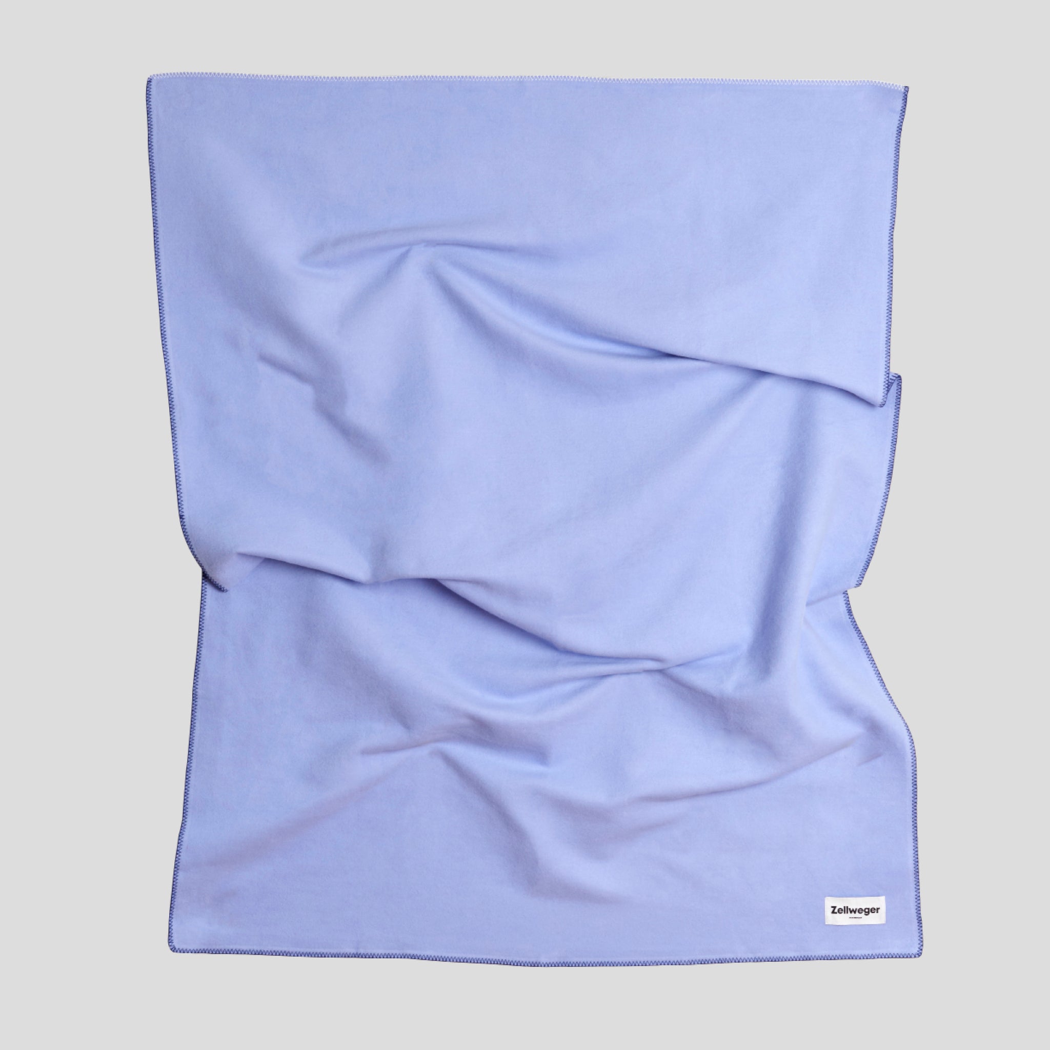 Faltiges, hellblaues Tuch mit sichtbarem Markenetikett in der unteren rechten Ecke.