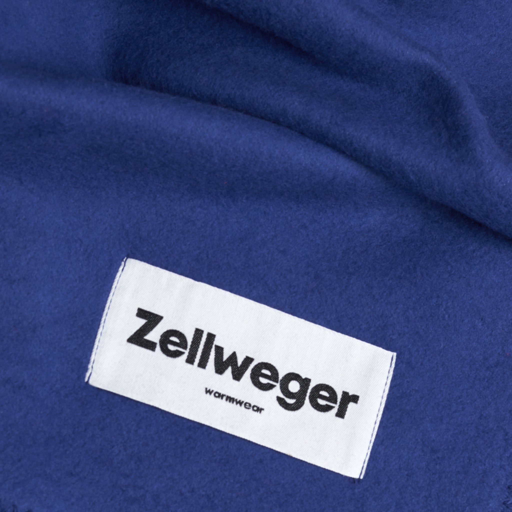 Blauer Stoff mit einem weißen Etikett, das "Zellweger" und "warmwear" in schwarzem Text zeigt.