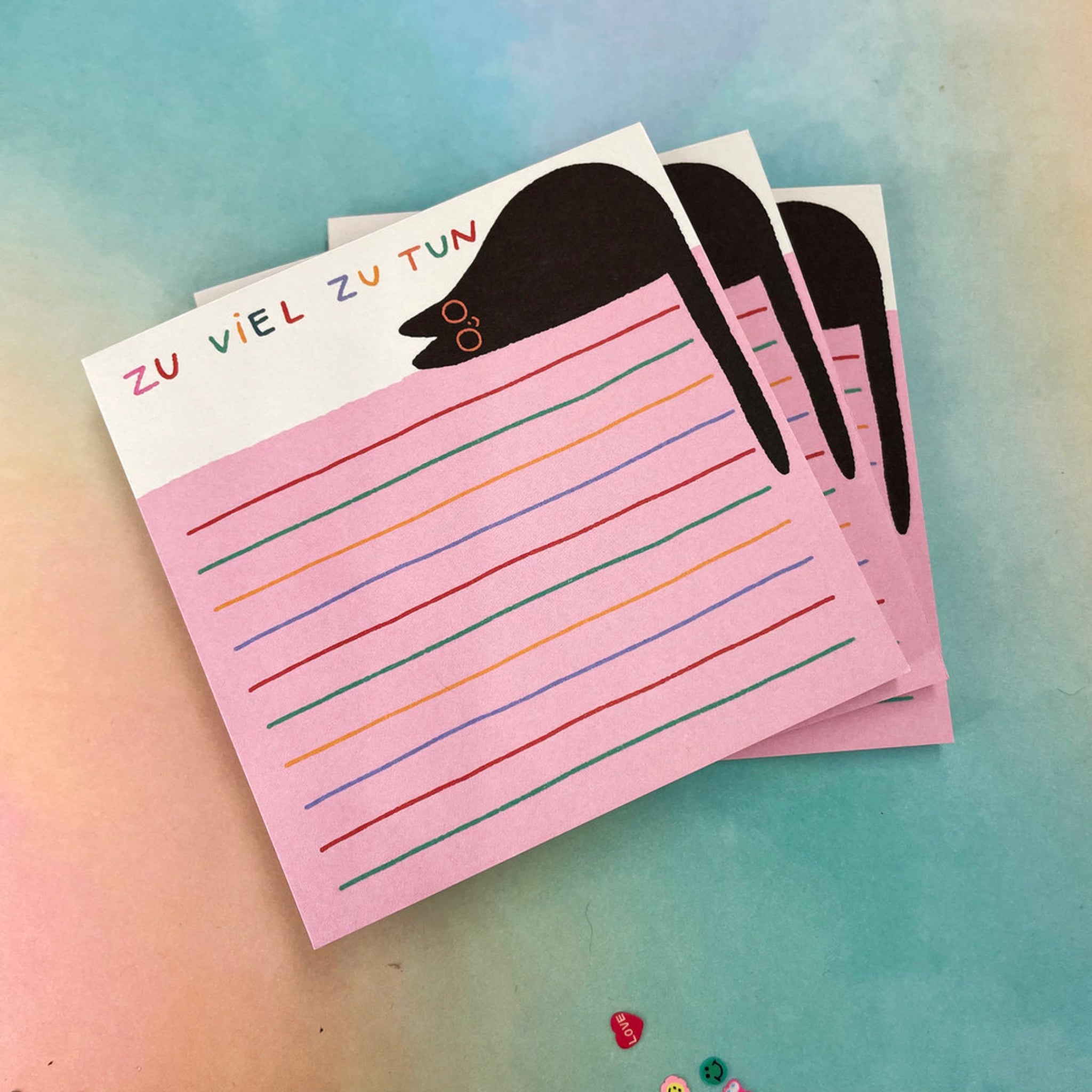 Drei rosa Notizblöcke mit "ZU VIEL ZU TUN", bunten Linien und einem Maulwurf, auf einem bunten Hintergrund.