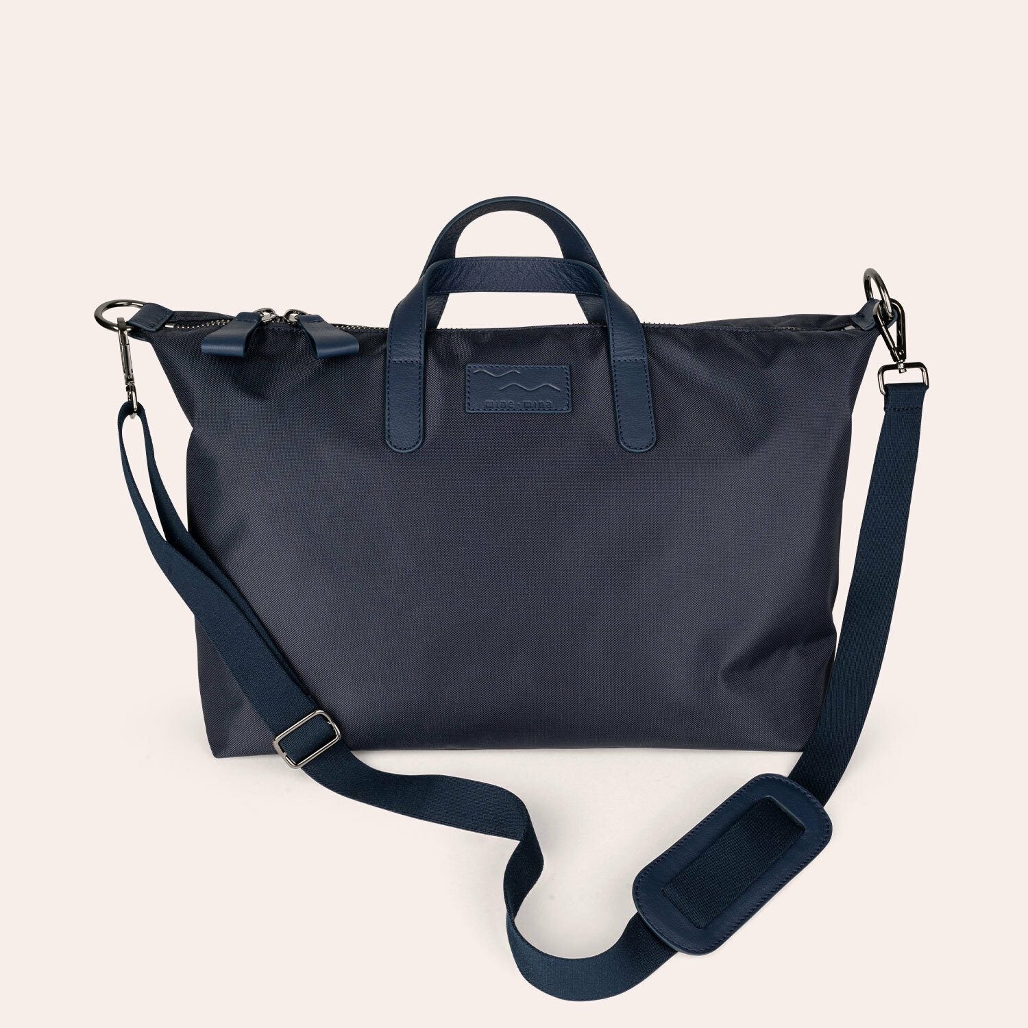 Ein marineblauer Seesack mit Ledergriffen, einem abnehmbaren Schulterriemen und einem Reißverschluss, der vor einem hellen Hintergrund dargestellt ist.