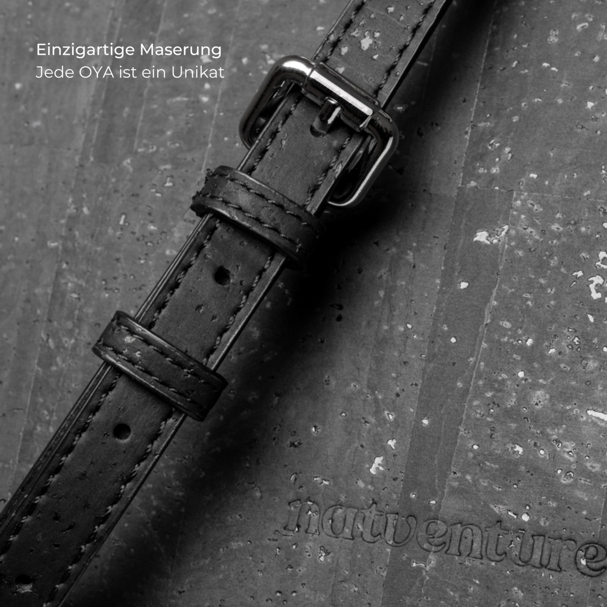 Schwarzes Lederarmband mit Metallschließe auf einer strukturierten Oberfläche, daneben der Text "Einzigartige Maserung".
