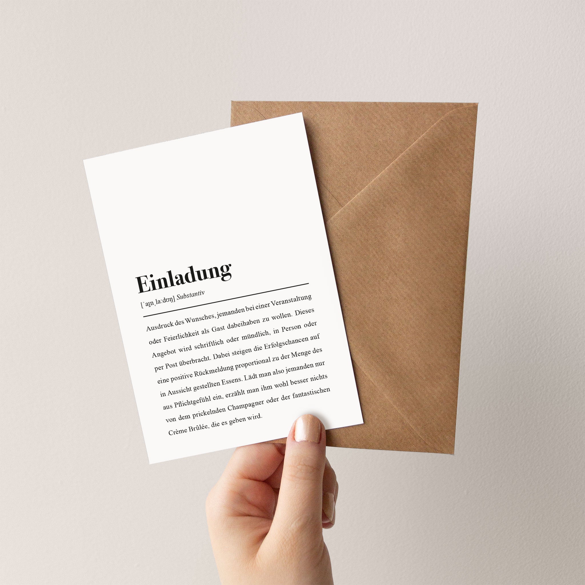 Hand hält eine Einladungskarte vor einem braunen Umschlag.