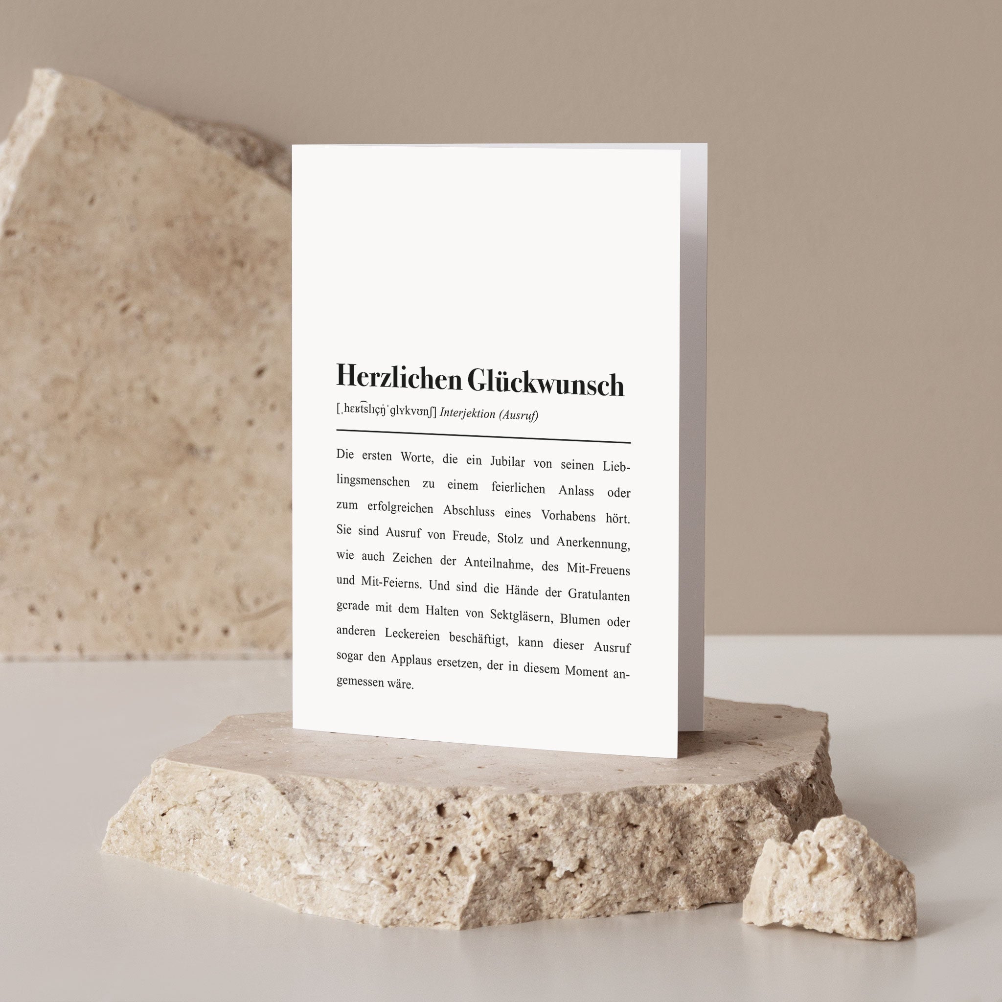 Eine weiße Karte mit der Aufschrift „Herzlichen Glückwunsch“ steht auf einem hellen Steinblock.