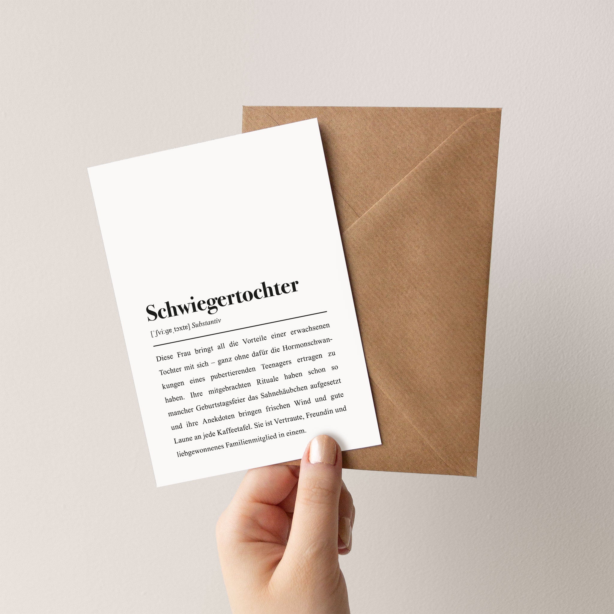 Hand hält eine Karte mit Definition von "Schwiegertochter", neben einem braunen Umschlag.