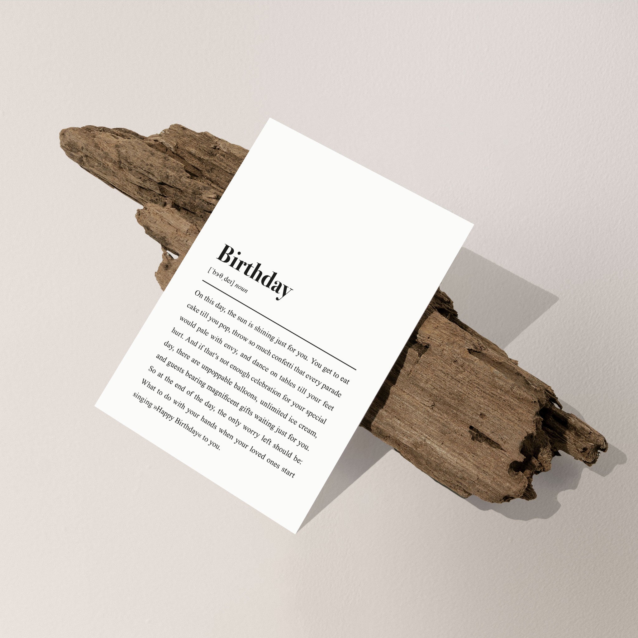 Eine weiße Karte mit einem Gedicht mit dem Titel "Birthday" liegt auf einem Stück Holz vor einem hellen Hintergrund.
