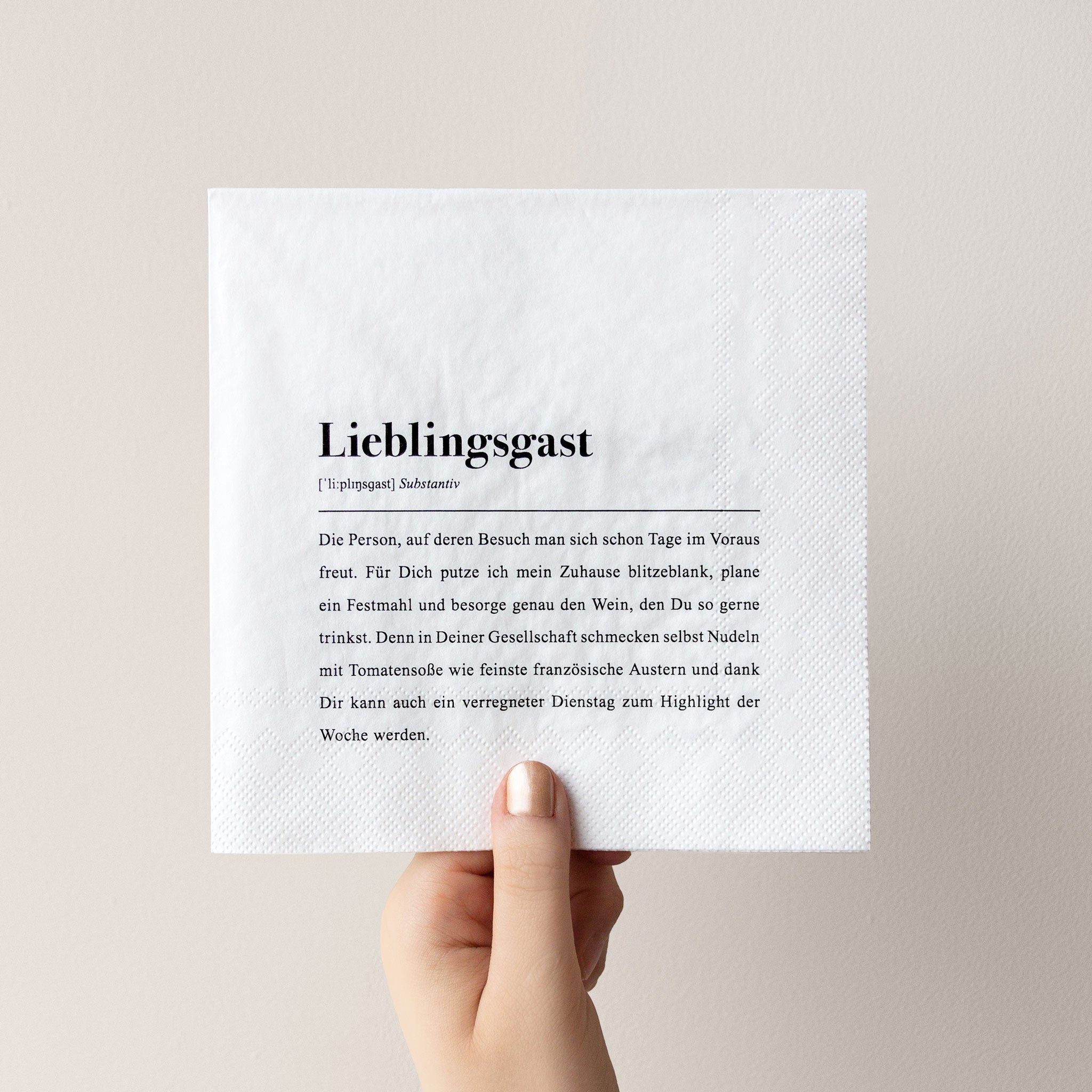 Eine Hand hält eine Serviette mit dem gedruckten Text "Lieblingsgast" und einer liebevollen Beschreibung dazu.