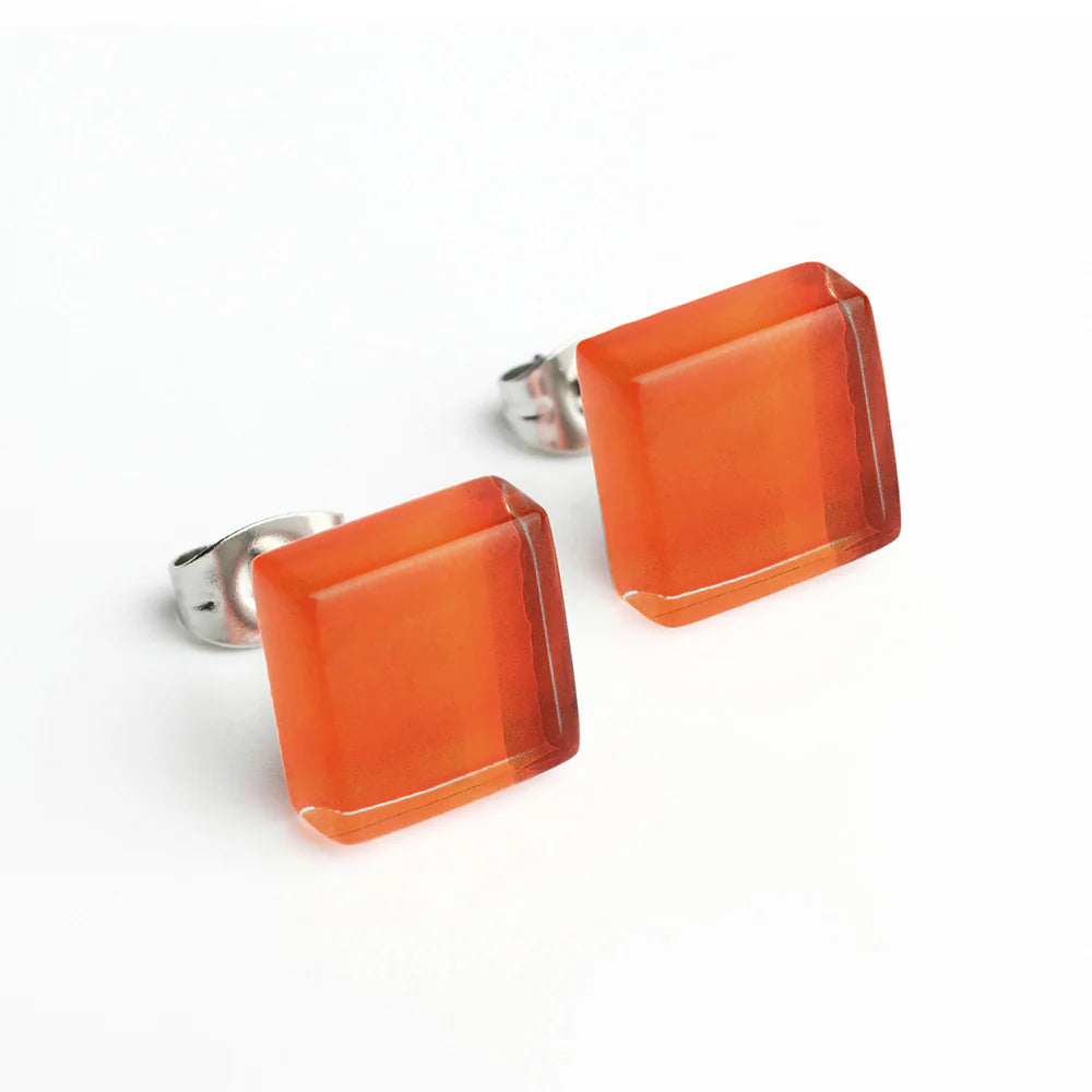 Ein Paar quadratische orangefarbene Ohrstecker mit glänzender Oberfläche und silberner Metallrückseite auf weißem Hintergrund.