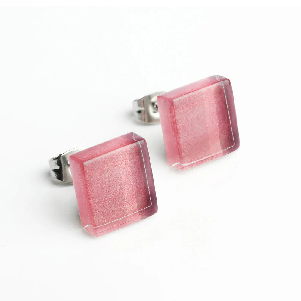 Ein Paar quadratische Ohrstecker mit rosa Farbverlauf und glänzender, leicht transparenter Oberfläche, die auf silberfarbenen Metallstiften vor weißem Hintergrund sitzen.