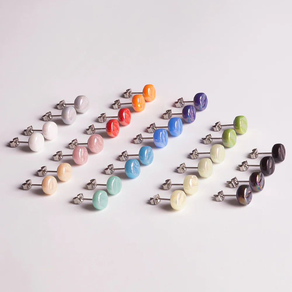 Ein fein säuberlich angeordnetes Set von zwanzig Paar farbigen Ohrsteckern auf einer weißen Oberfläche, mit einer Vielzahl von Farben wie weiß, rosa, rot, orange, blau, grün, lila und schwarz.