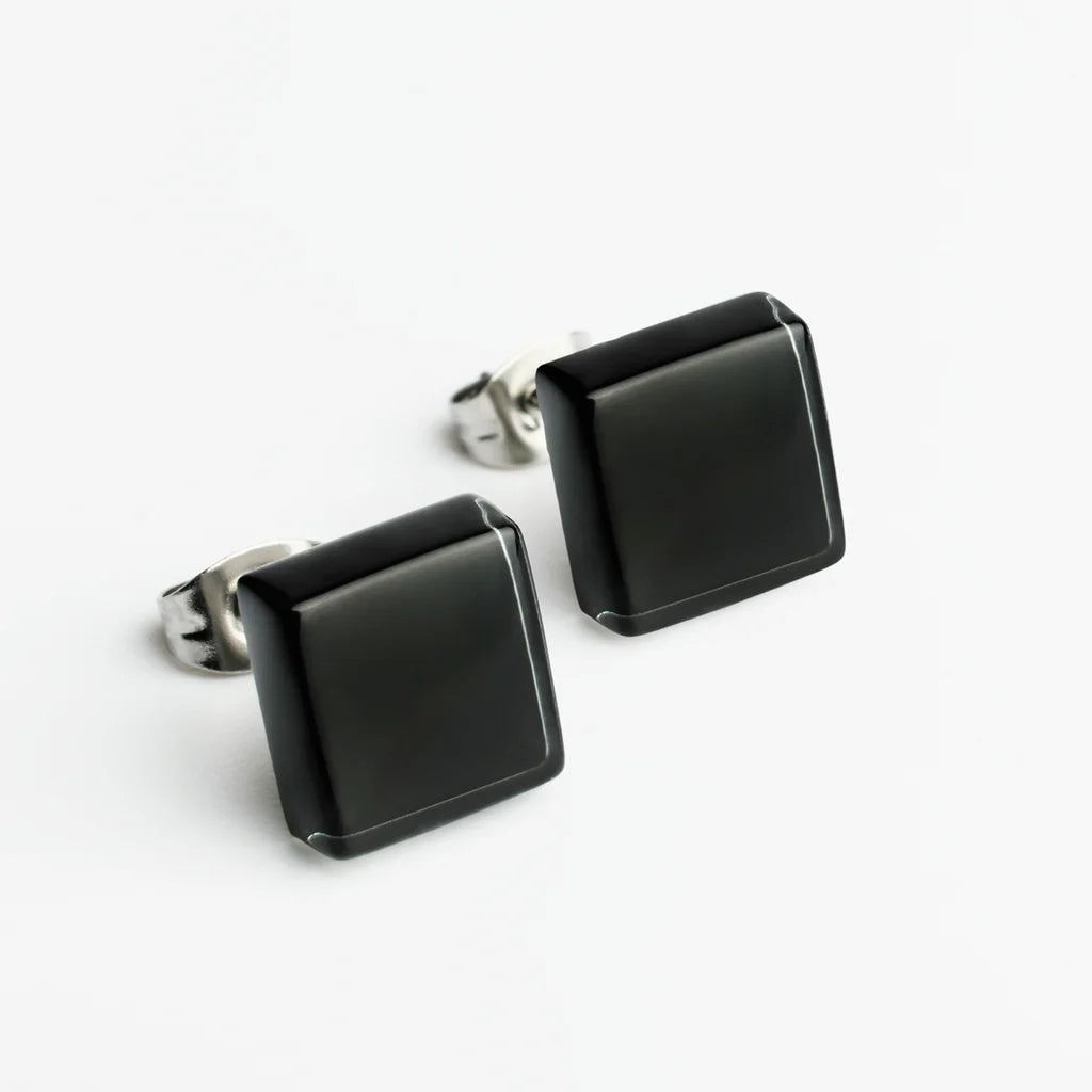 Ein Paar quadratische Ohrstecker aus schwarzen Steinen mit Metallrückseite auf weißem Hintergrund.